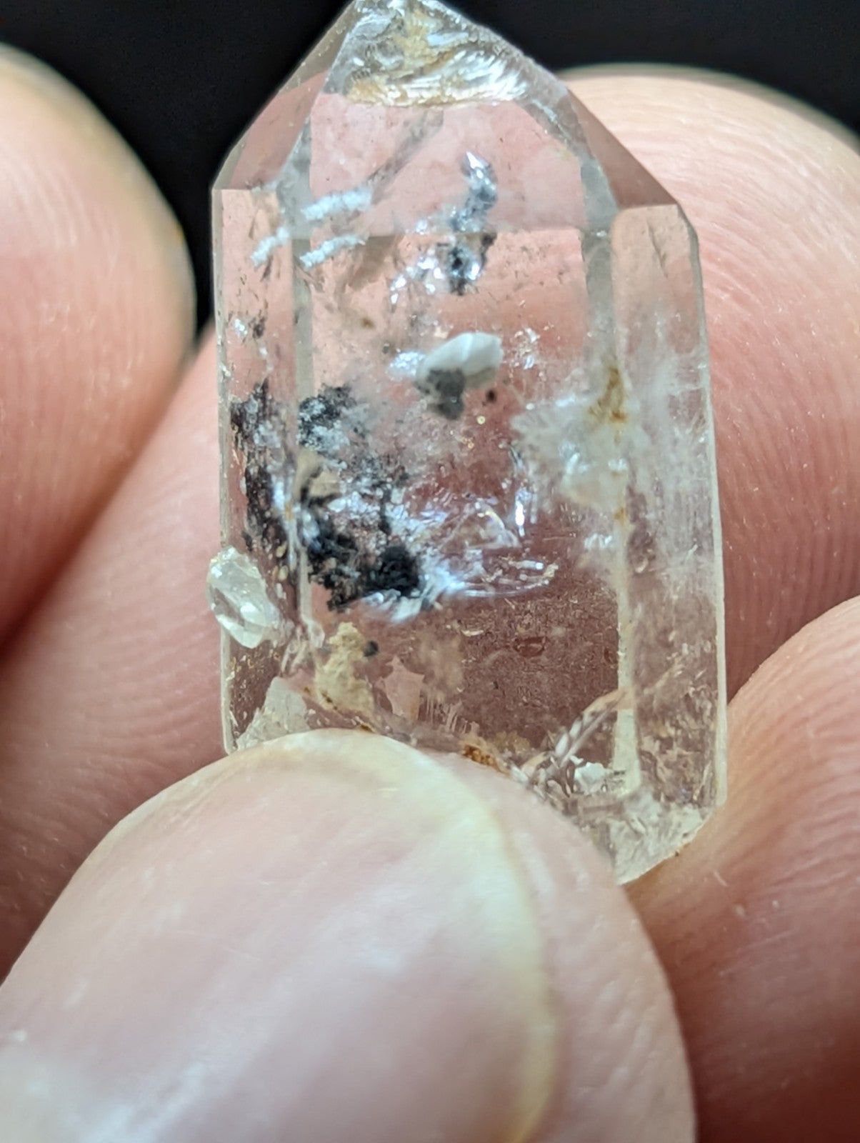 A clear quartz crystal with natural inclusions and a pointed, faceted top.