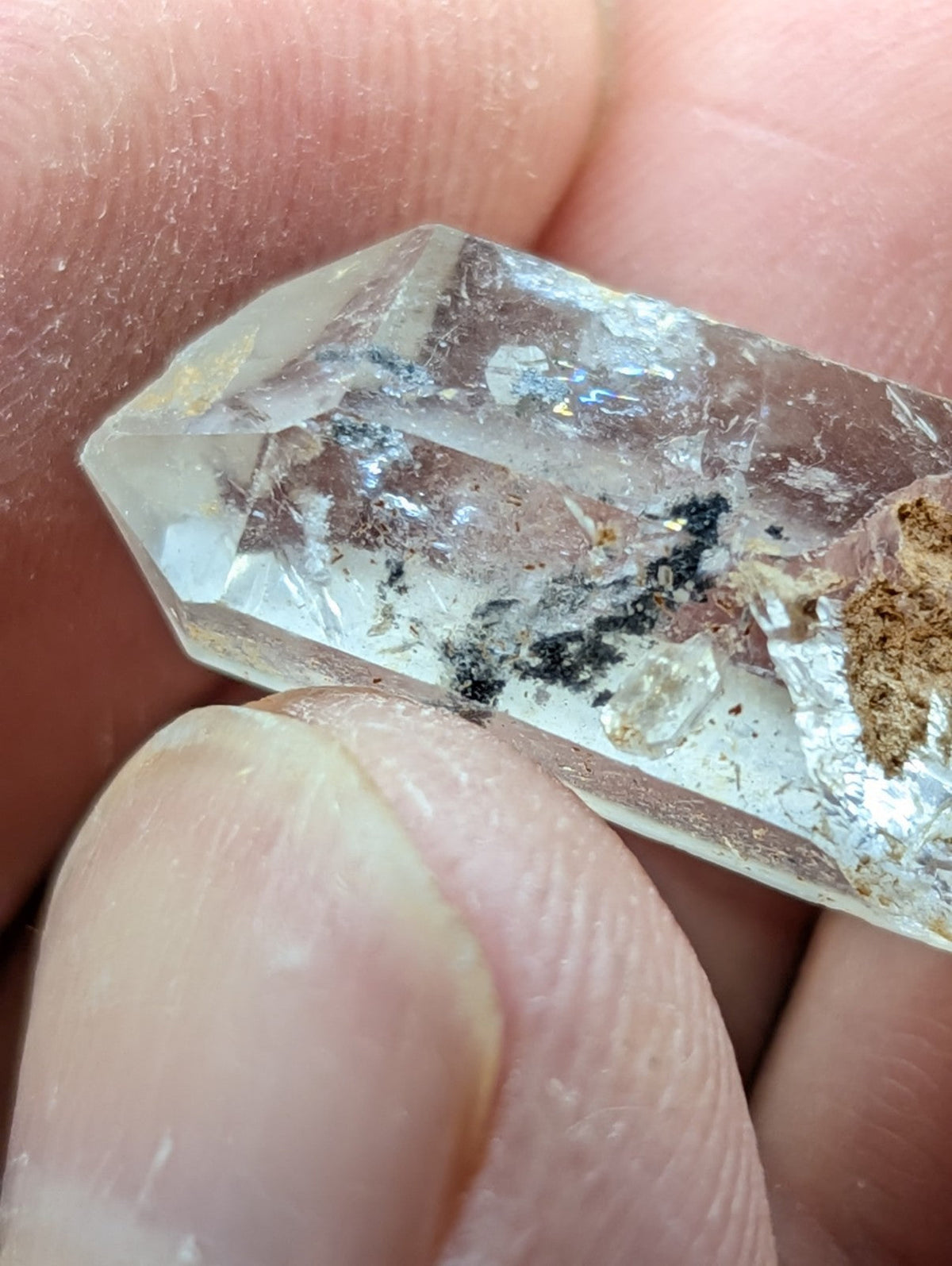 A clear, faceted quartz crystal with natural inclusions and earthy residue on its surface.