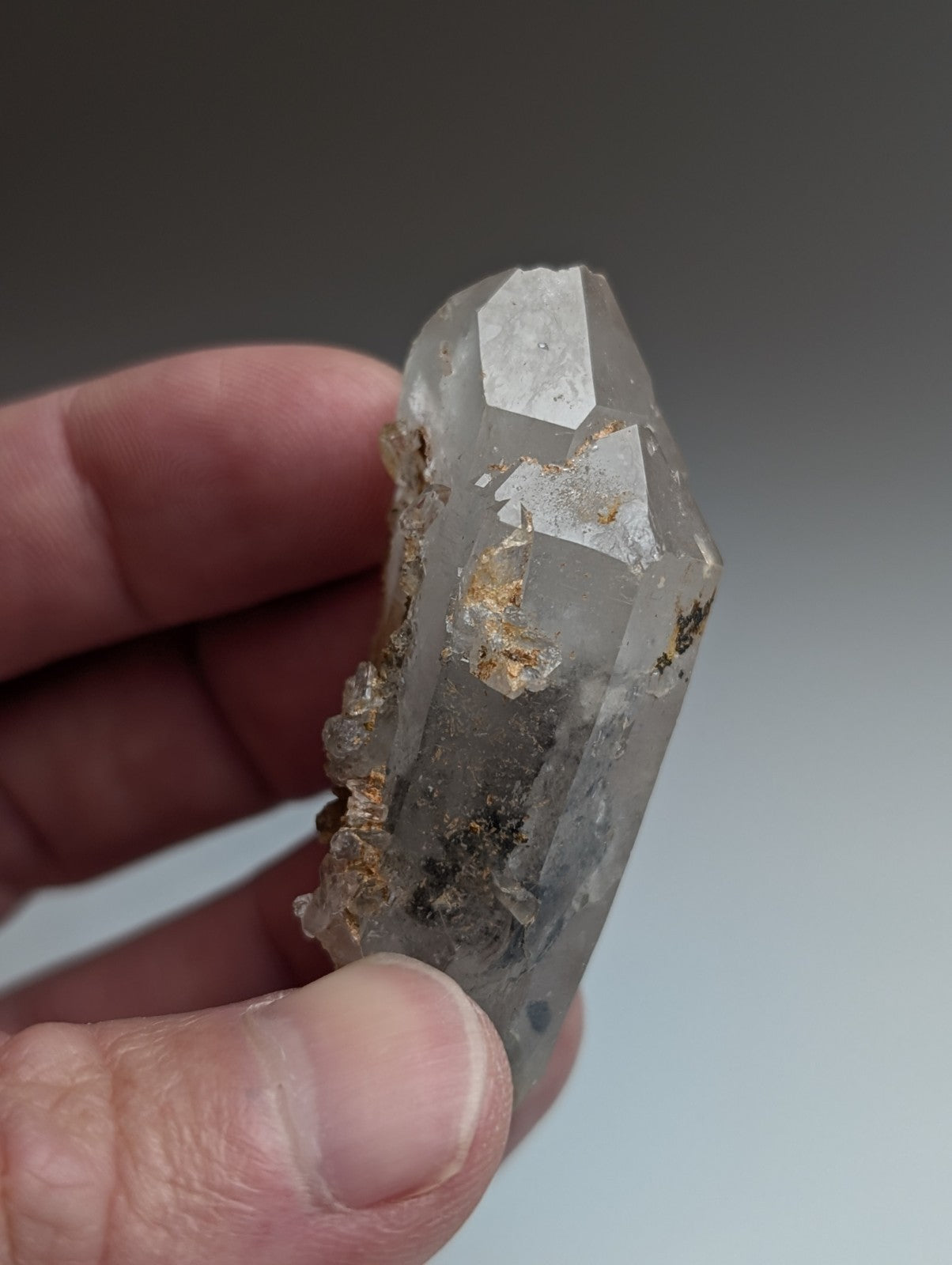 A translucent quartz crystal with nacrite mineral inclusions held gently between fingers from montgomery county arkansas