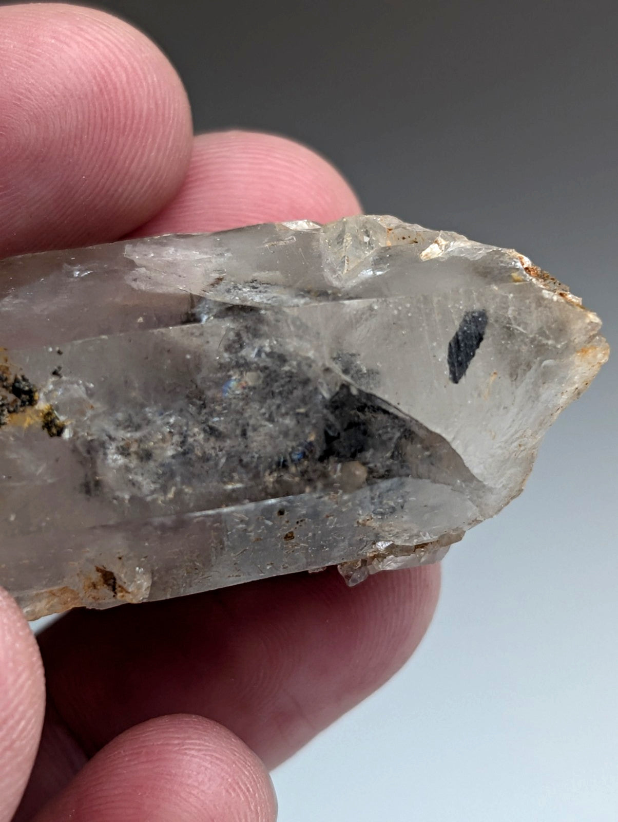 A translucent quartz crystal with nacrite inclusions and a pointed tip held gently between fingers from Arkansas