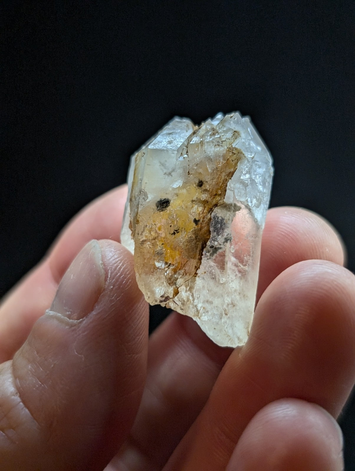 A translucent, pale quartz crystal with a rough, jagged surface and embedded yellowish-brown inclusions.