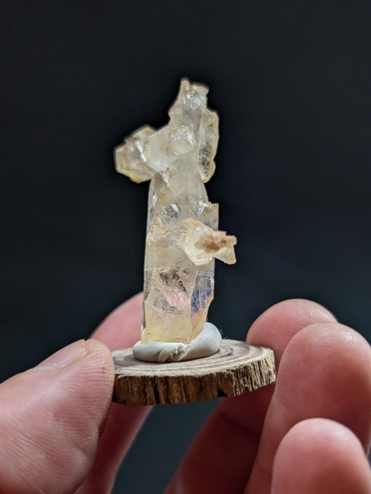 A translucent, pale yellow crystal formation with jagged edges and internal inclusions stands upright on a rustic wooden slice base.