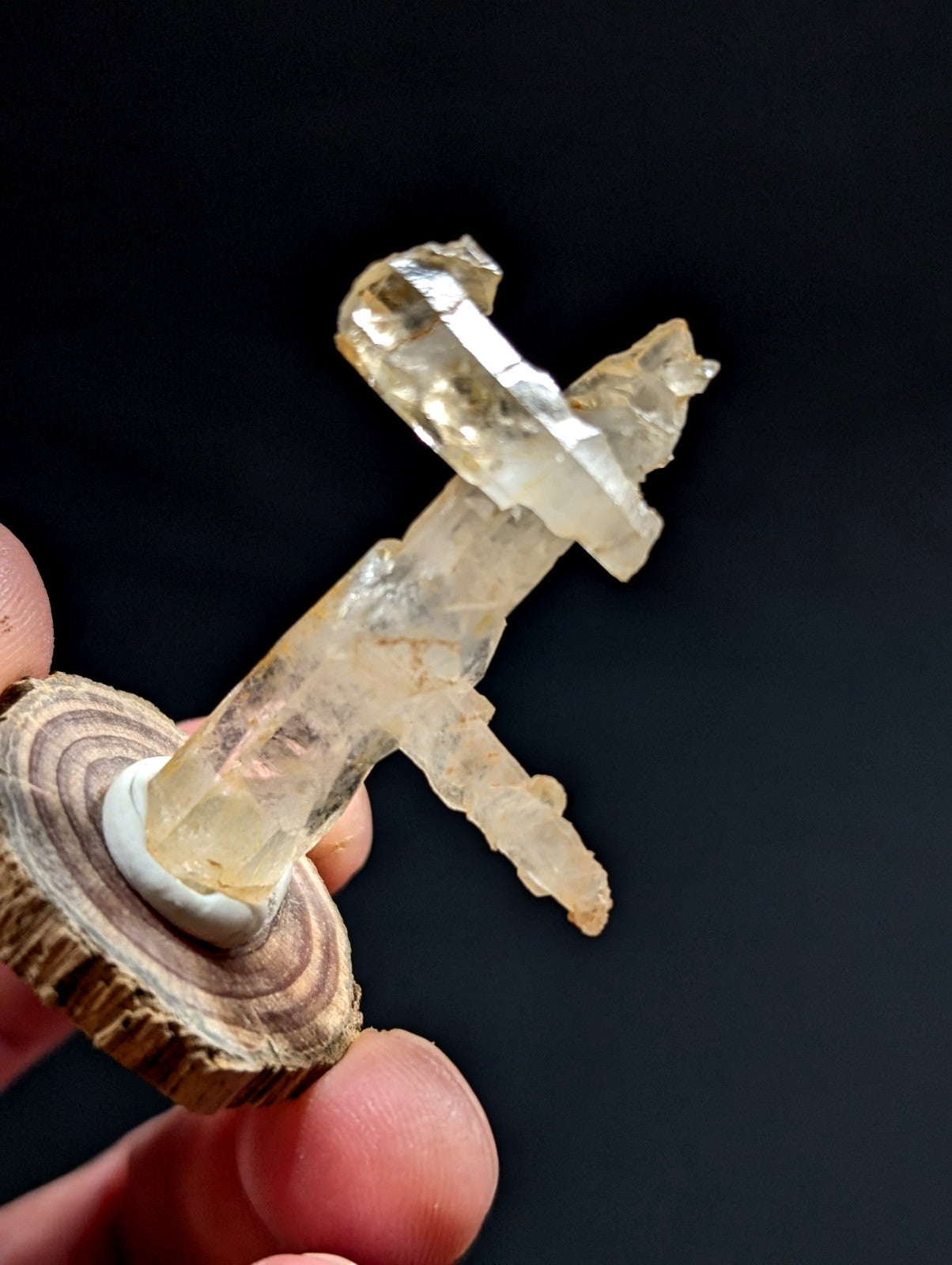 A translucent, pale yellow crystal formation with natural facets and a rough, jagged top is mounted on a circular wooden slice base.