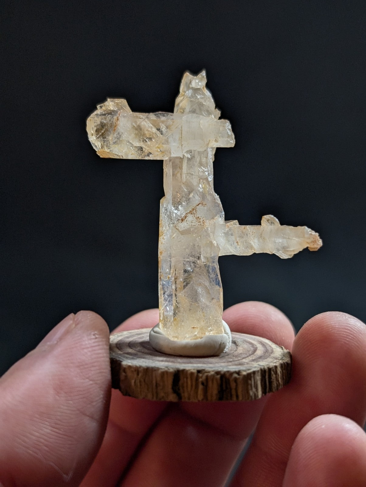 A translucent, pale yellow crystal figurine with a natural, rough-edged texture and crystalline facets stands on a circular wooden base.