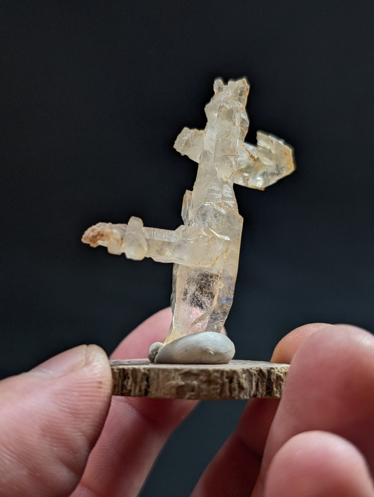 A translucent, pale yellow crystal figurine of a standing figure with outstretched arms and legs, mounted on a rustic wooden base.