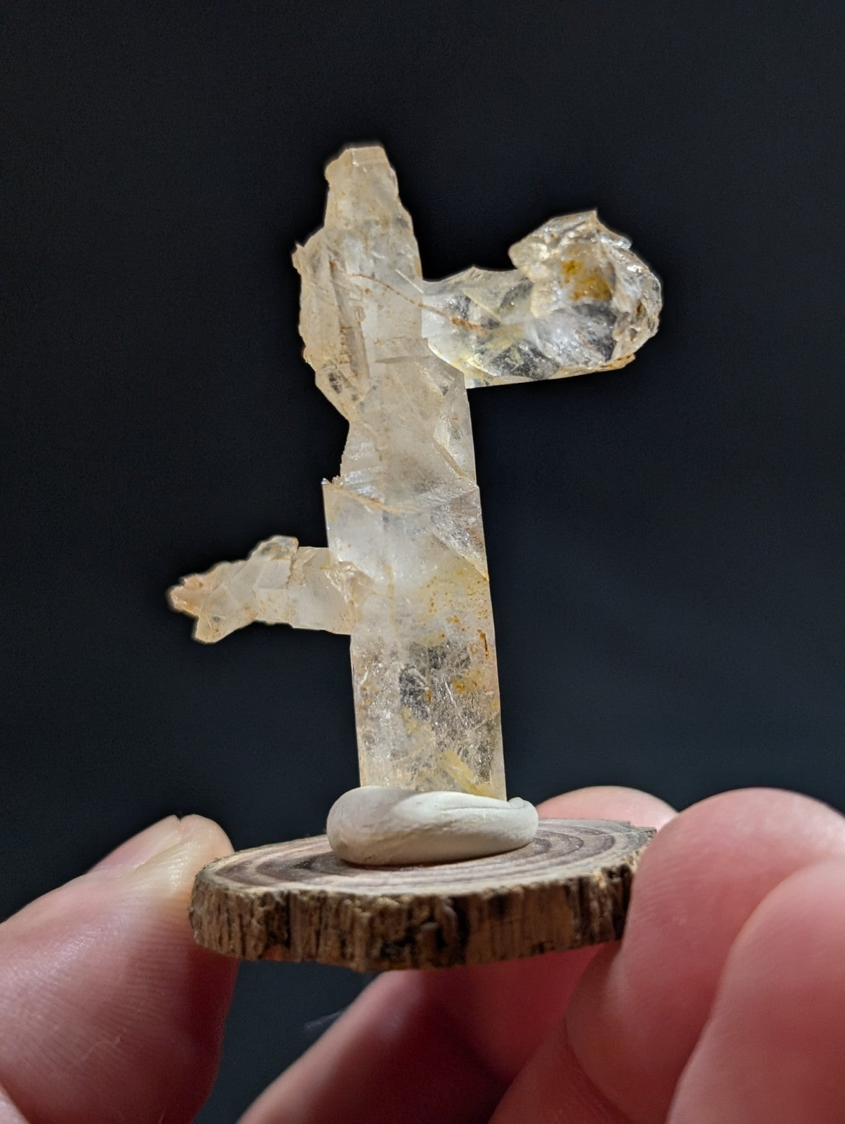 A translucent, pale yellow crystal formation with a rough, natural texture and irregular facets stands upright on a circular wooden base.