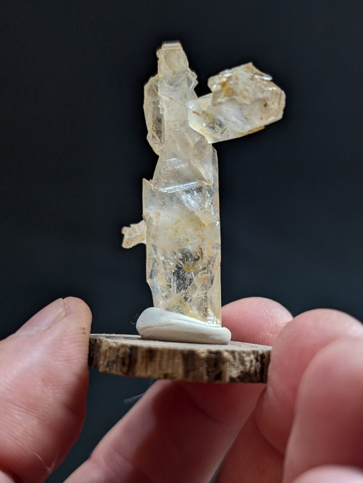 A translucent, pale yellow crystal figurine with jagged edges and natural inclusions stands on a rustic wooden base.