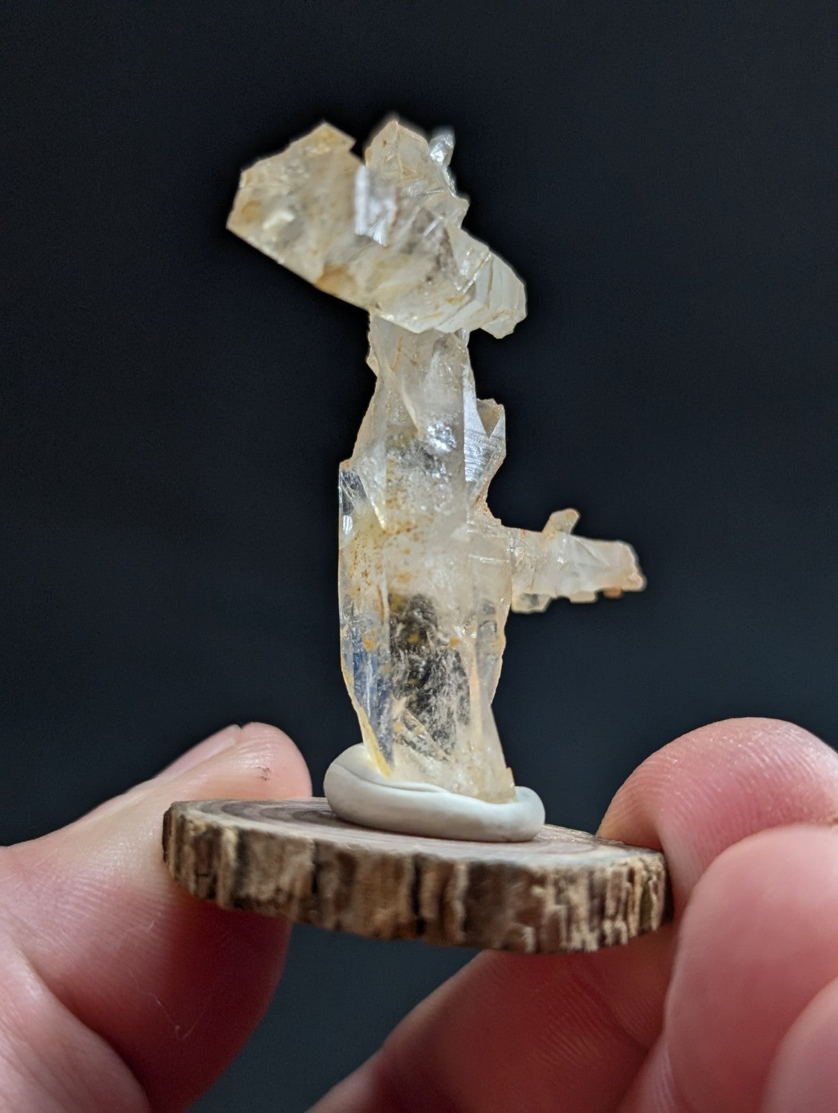 A translucent, pale yellow crystal formation with jagged edges and a natural, irregular shape stands on a rustic wooden base.