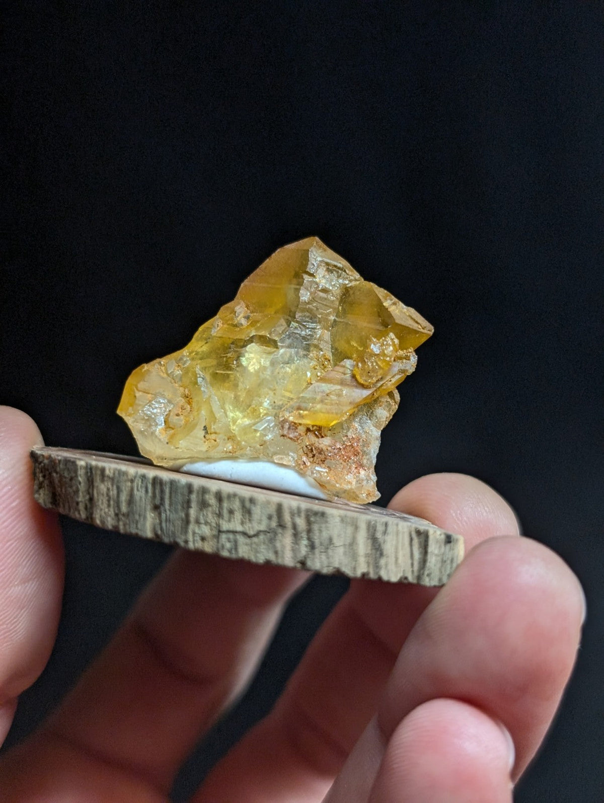 A translucent golden-yellow citrine crystal with a rough, faceted surface rests on a rustic wooden slice.