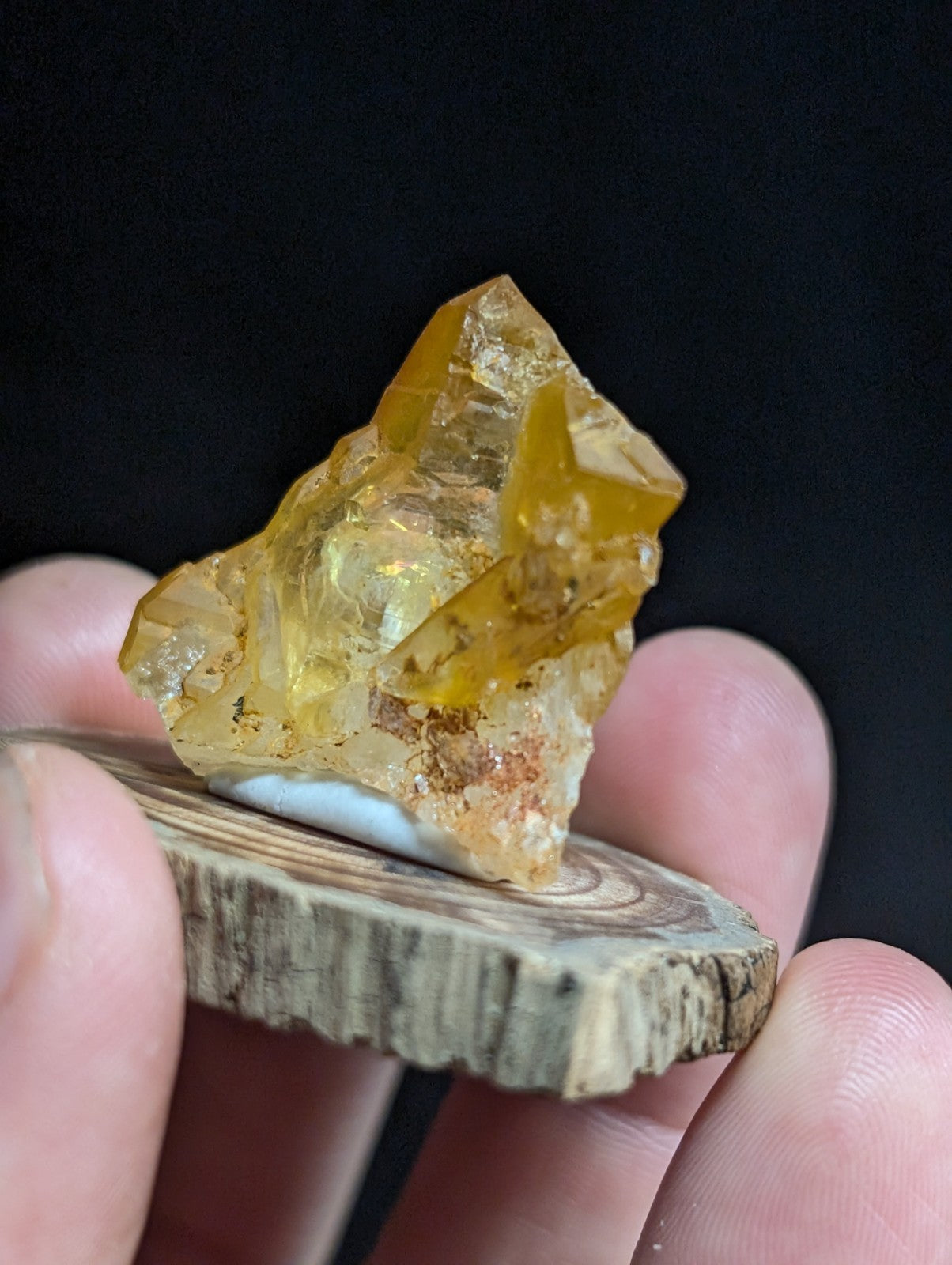 A translucent golden-yellow amber crystal with natural facets and embedded inclusions, resting on a rustic wooden slice.