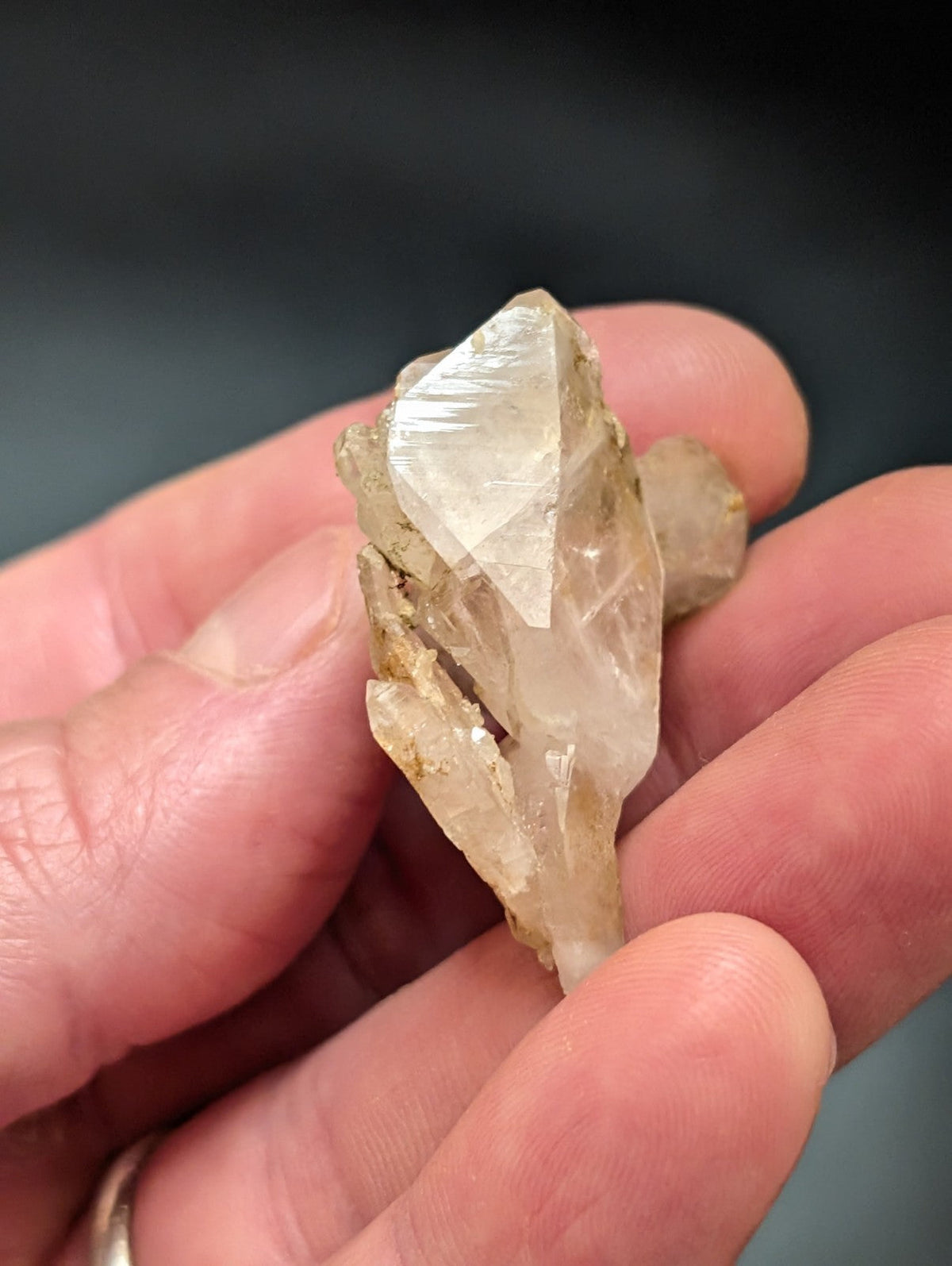 A translucent, pale quartz crystal with a faceted top and rougher base held in someone’s hand.