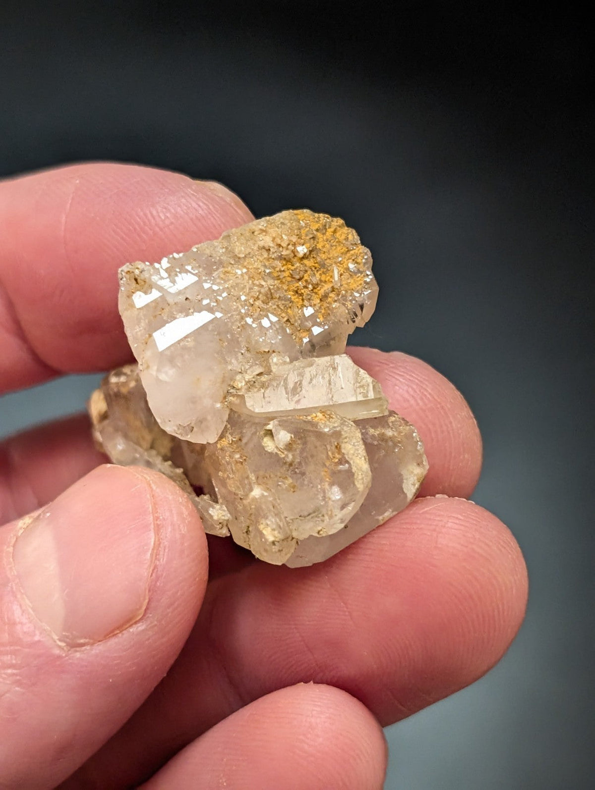 A translucent quartz crystal cluster with golden mineral inclusions, held gently between fingers.