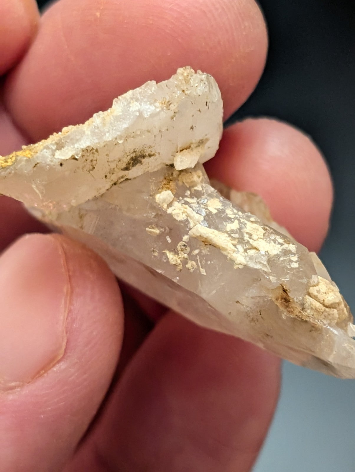 A translucent, pale quartz crystal with golden mineral inclusions and a rough, jagged surface.