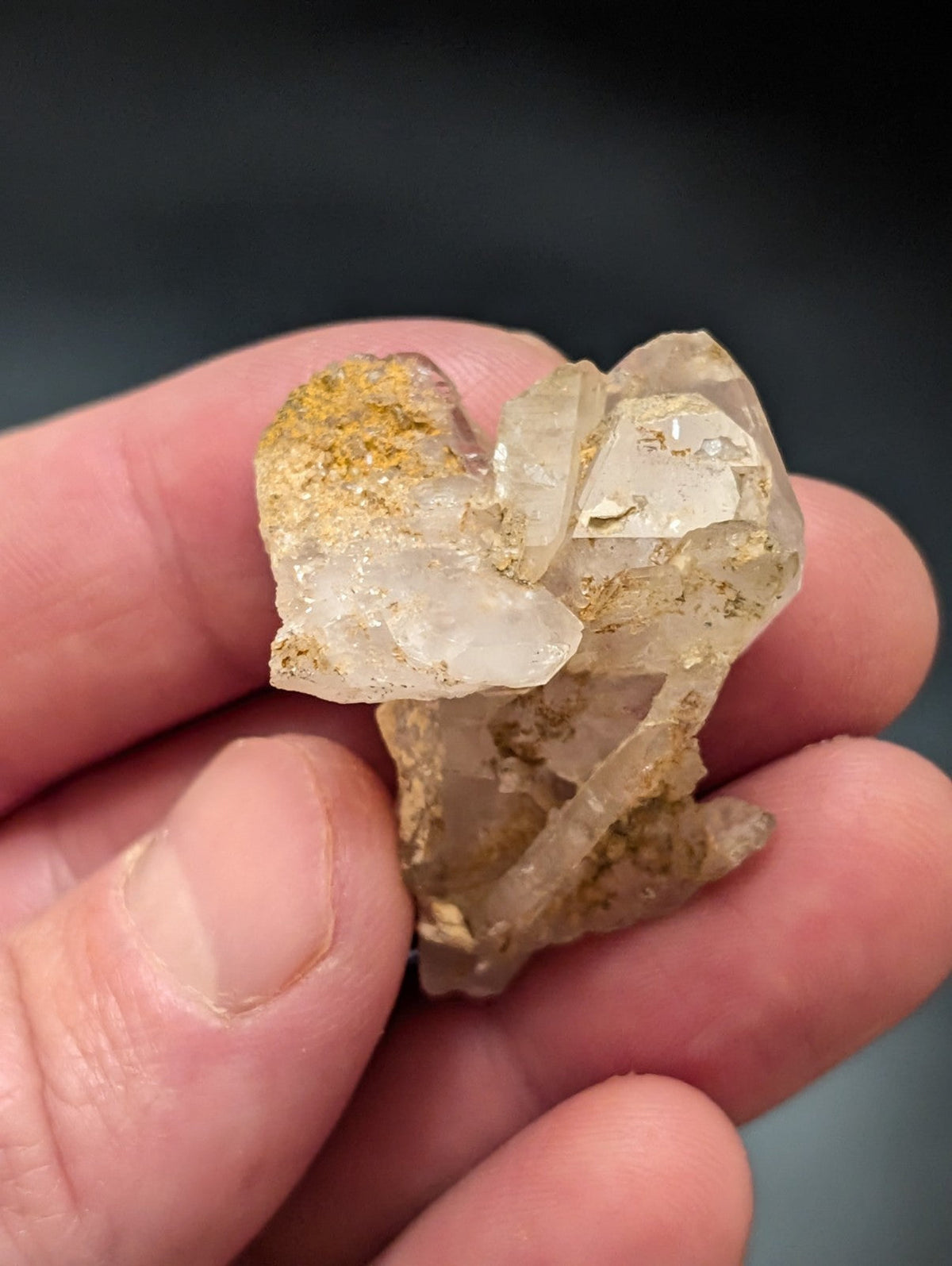 A translucent, crystalline quartz cluster with golden mineral inclusions held gently in a hand.