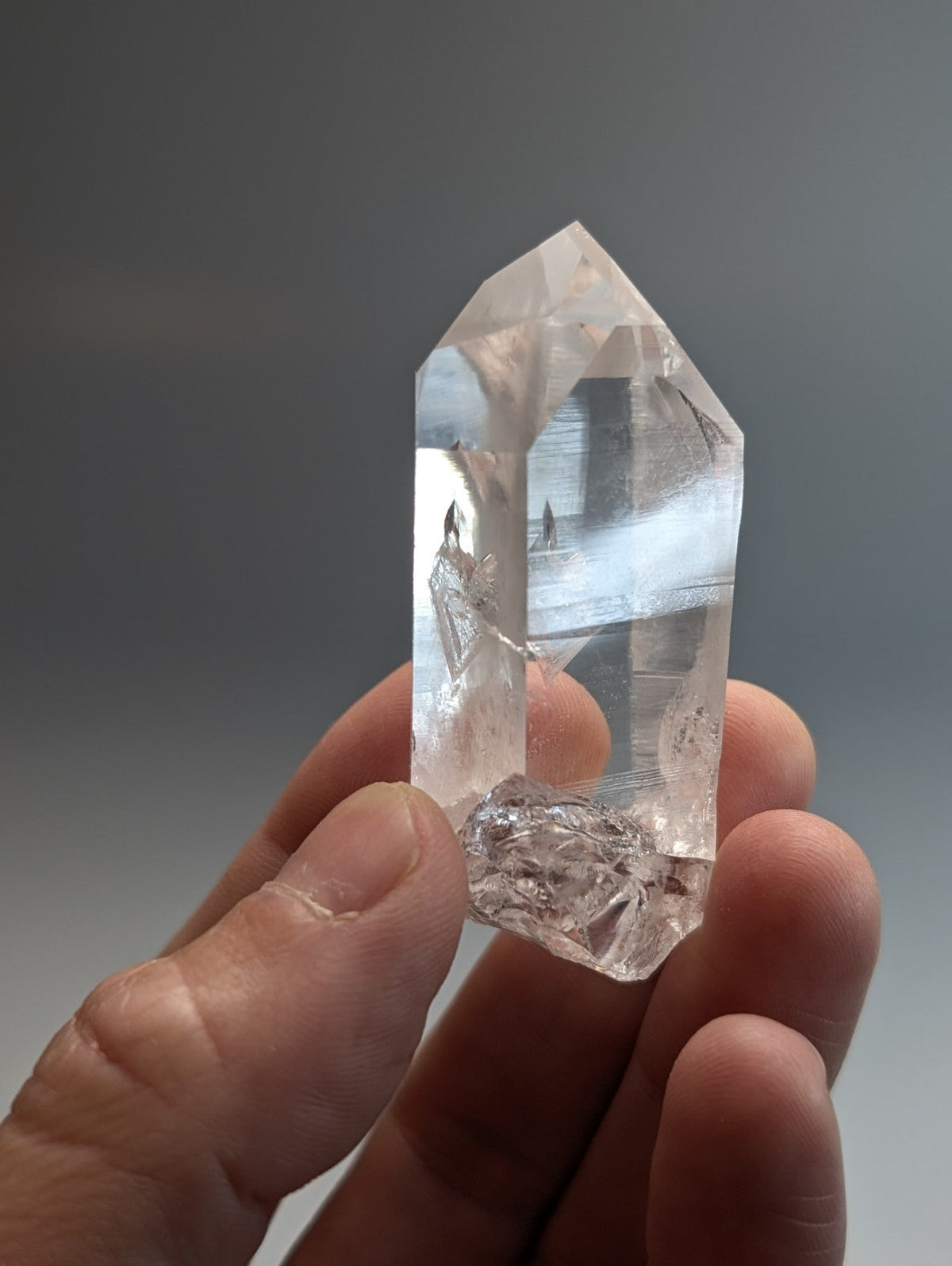 A clear faceted quartz crystal point with a pointed top and rough base held in hand from old stock arkansas usa