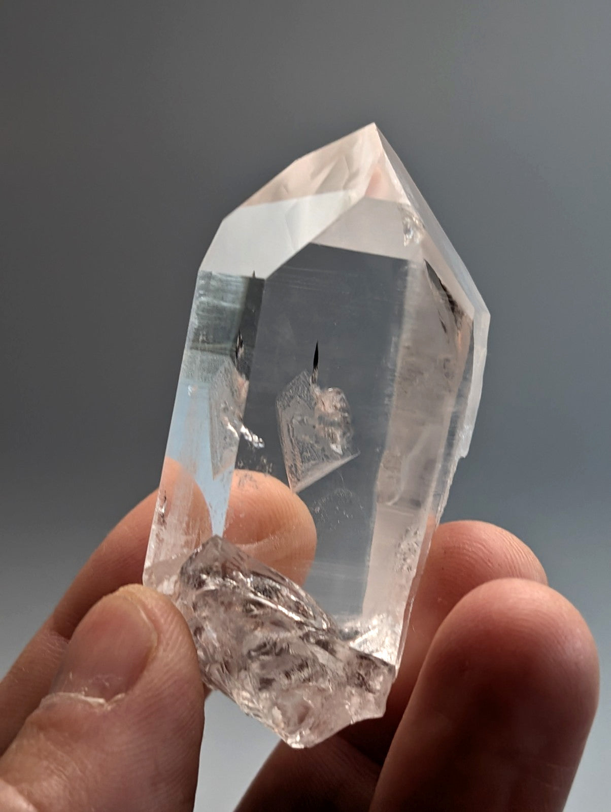 A clear transparent quartz crystal point with a rough base held in fingers unique old stock arkansas usa a plus water clear