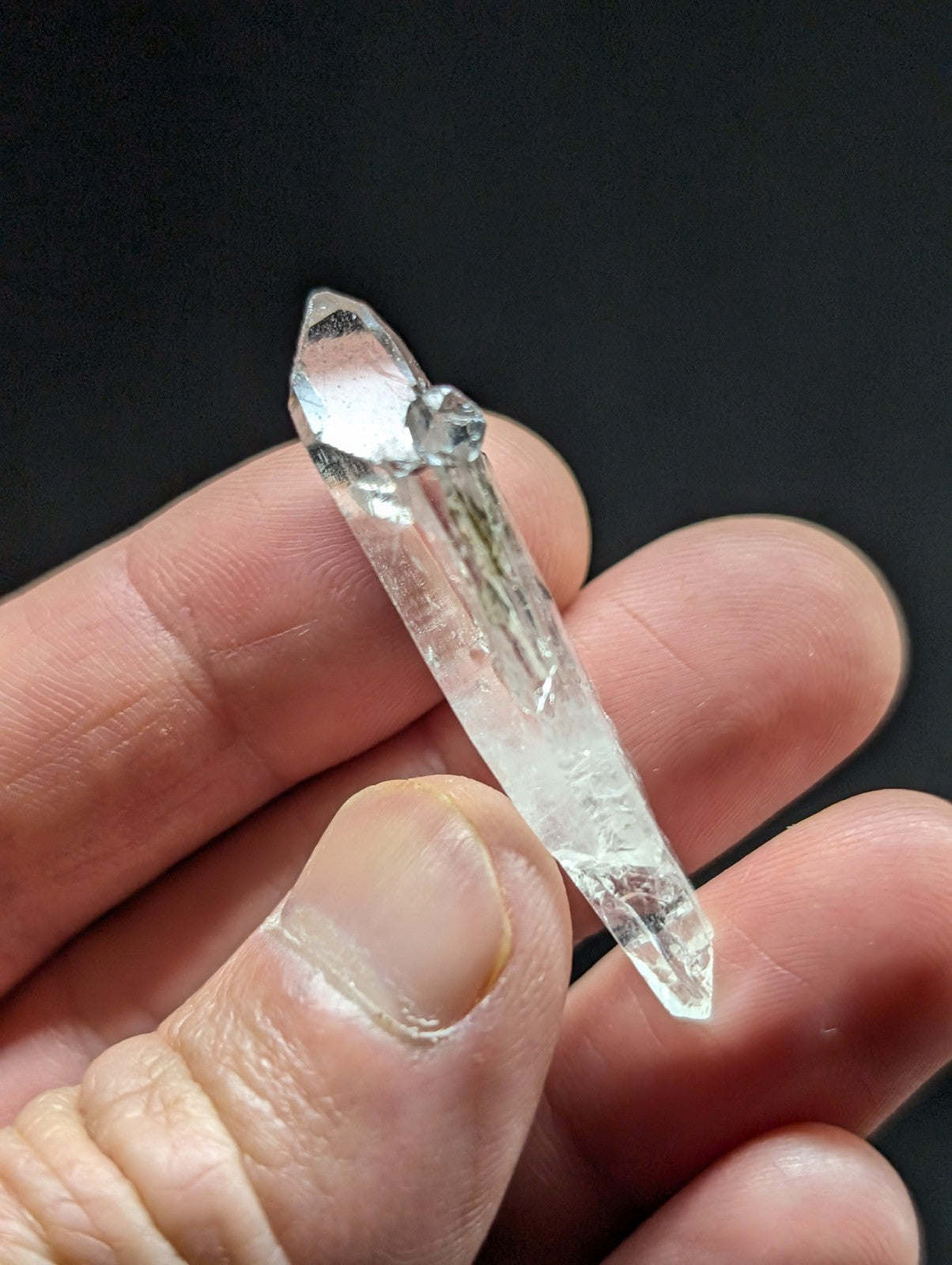 A clear quartz crystal with a pointed tip and visible internal inclusions, held delicately between fingers.