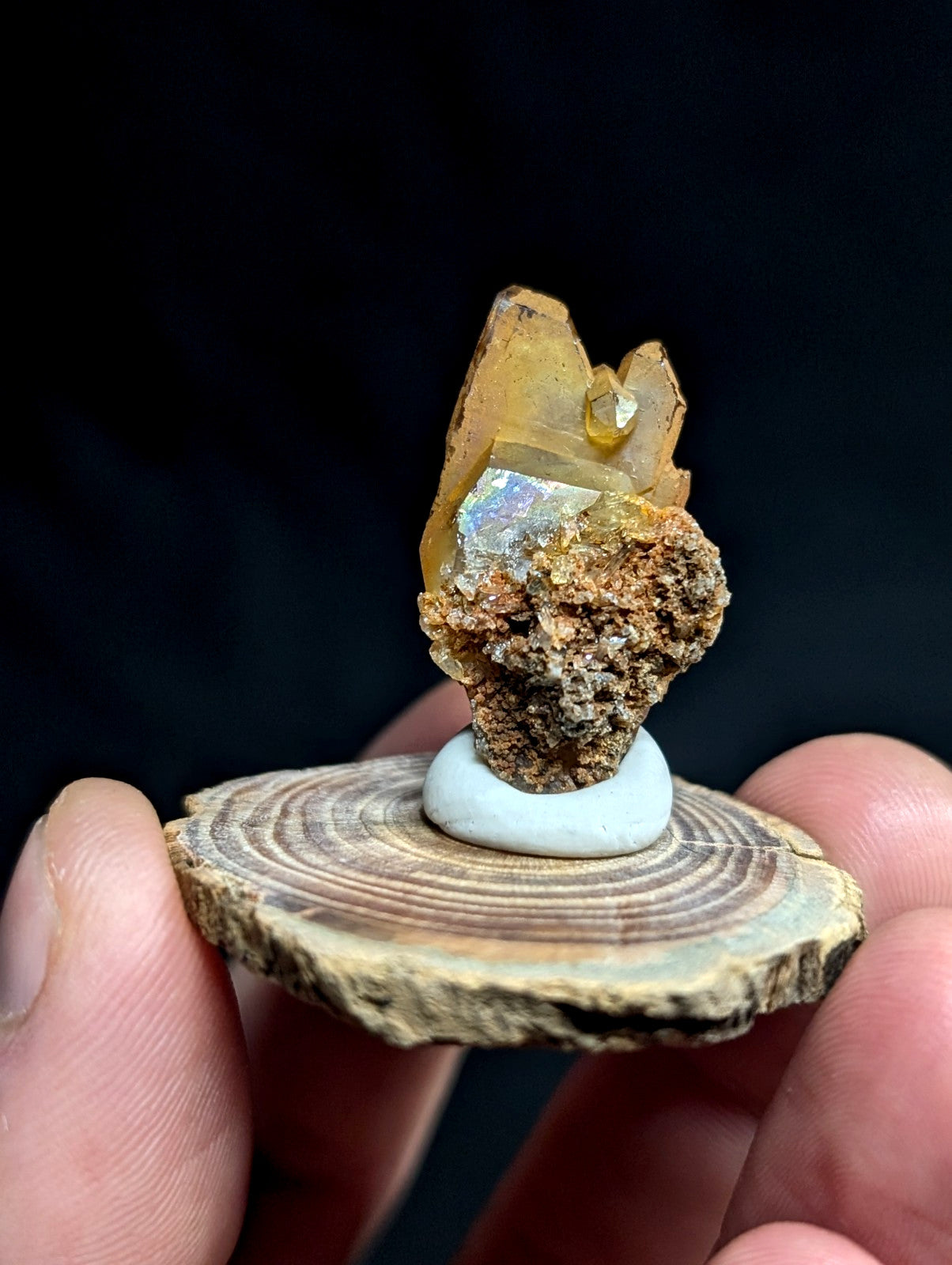 A polished amber-colored crystal specimen with a rough, earthy matrix base and iridescent facets.