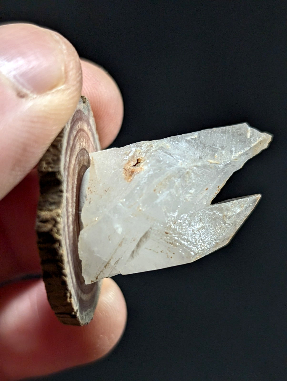 A translucent, faceted quartz crystal with a natural, jagged edge and subtle internal inclusions is held upright against a dark background.
