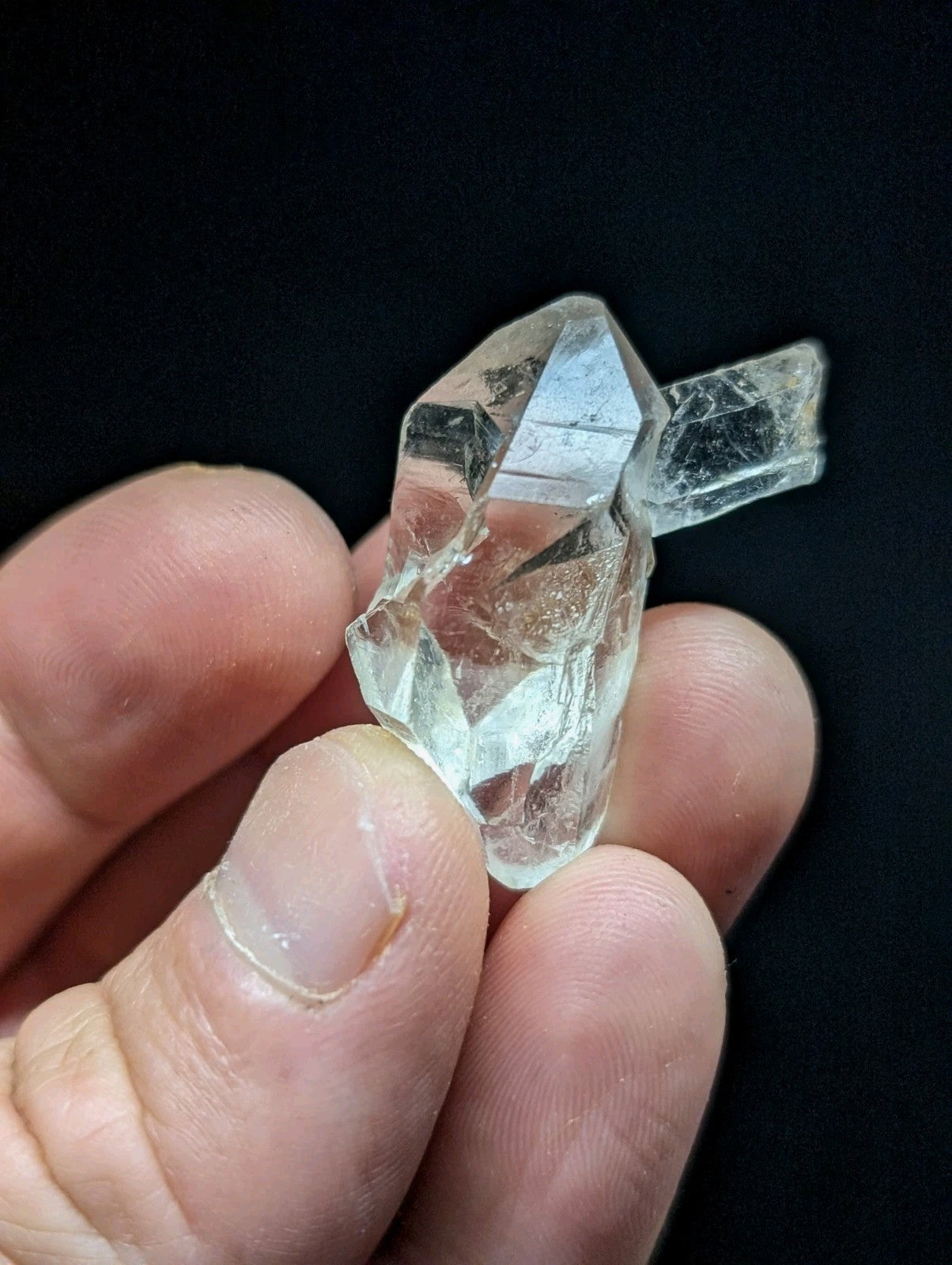 A clear, faceted quartz crystal cluster held gently in a hand.