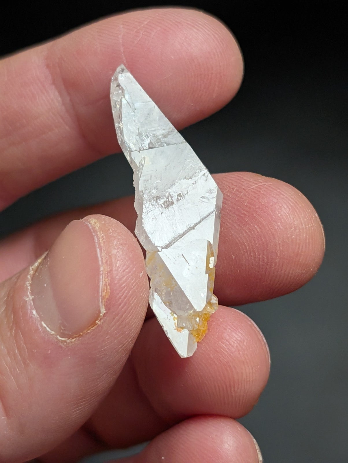 A translucent, clear quartz crystal with a pointed tip and subtle golden-yellow inclusions at its base.