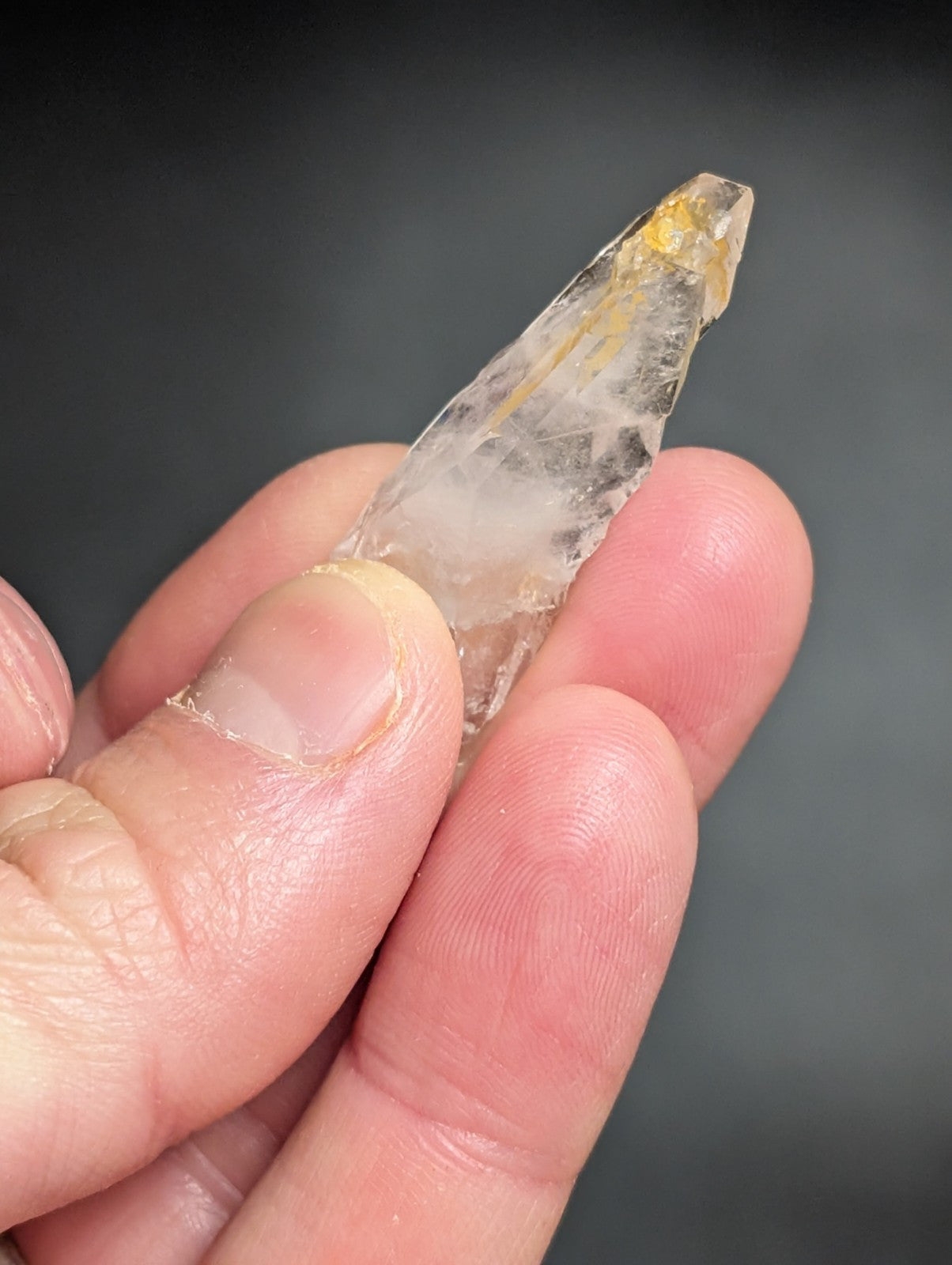 A translucent, pointed crystal with a subtle yellowish tint and natural internal inclusions.