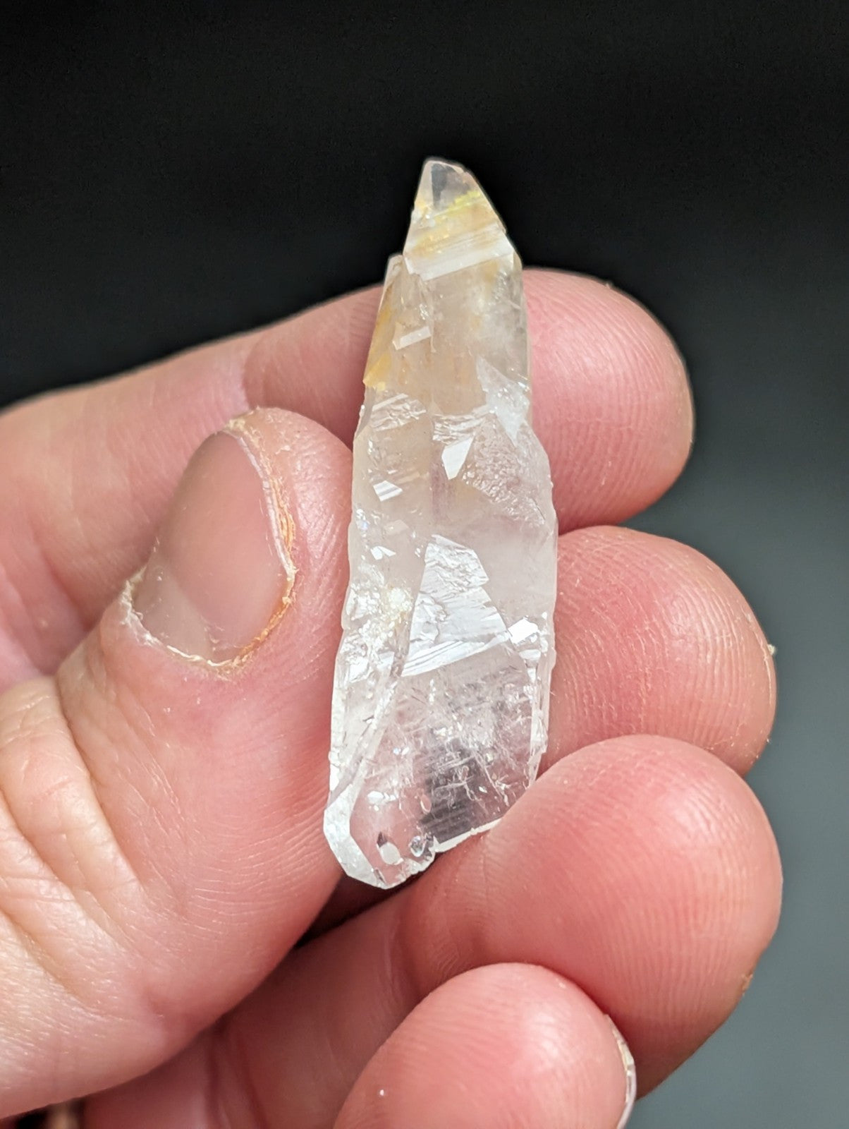 A translucent, clear quartz crystal with a pointed tip and subtle yellowish inclusions.