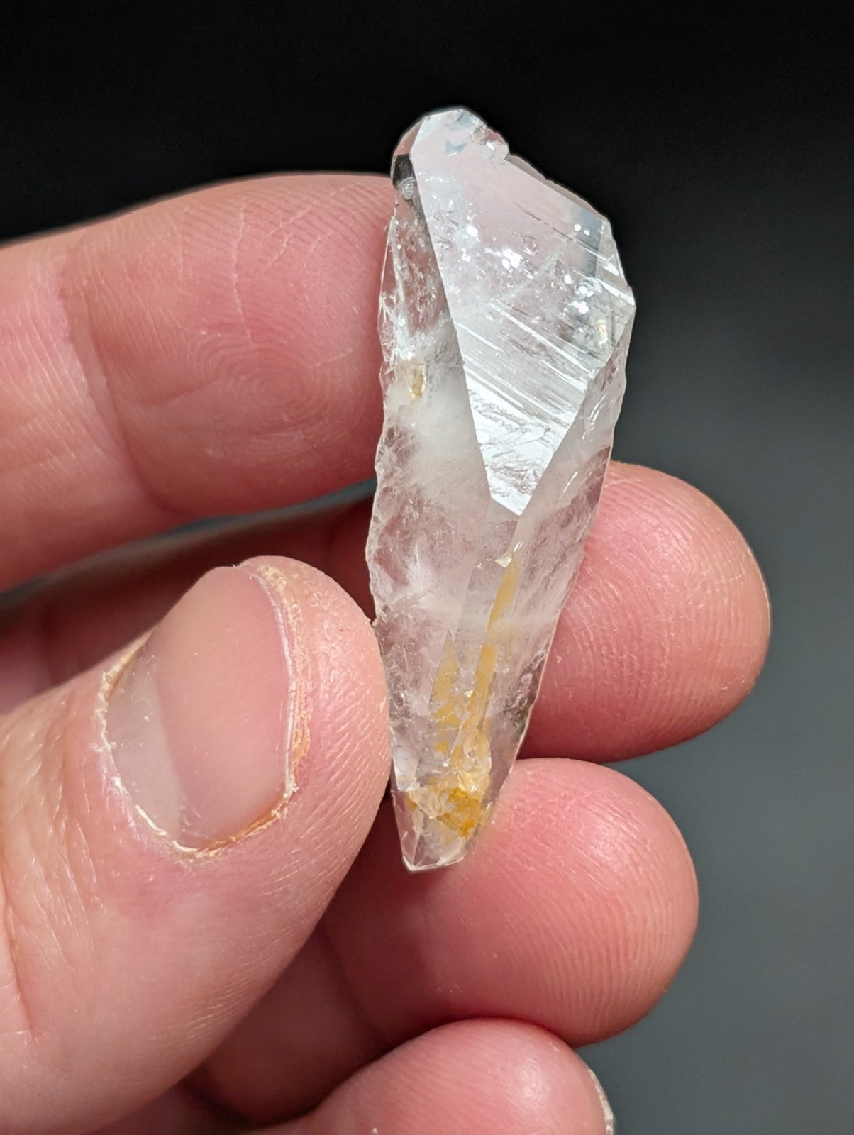 A translucent, clear quartz crystal with a pointed tip and subtle golden inclusions near its base.