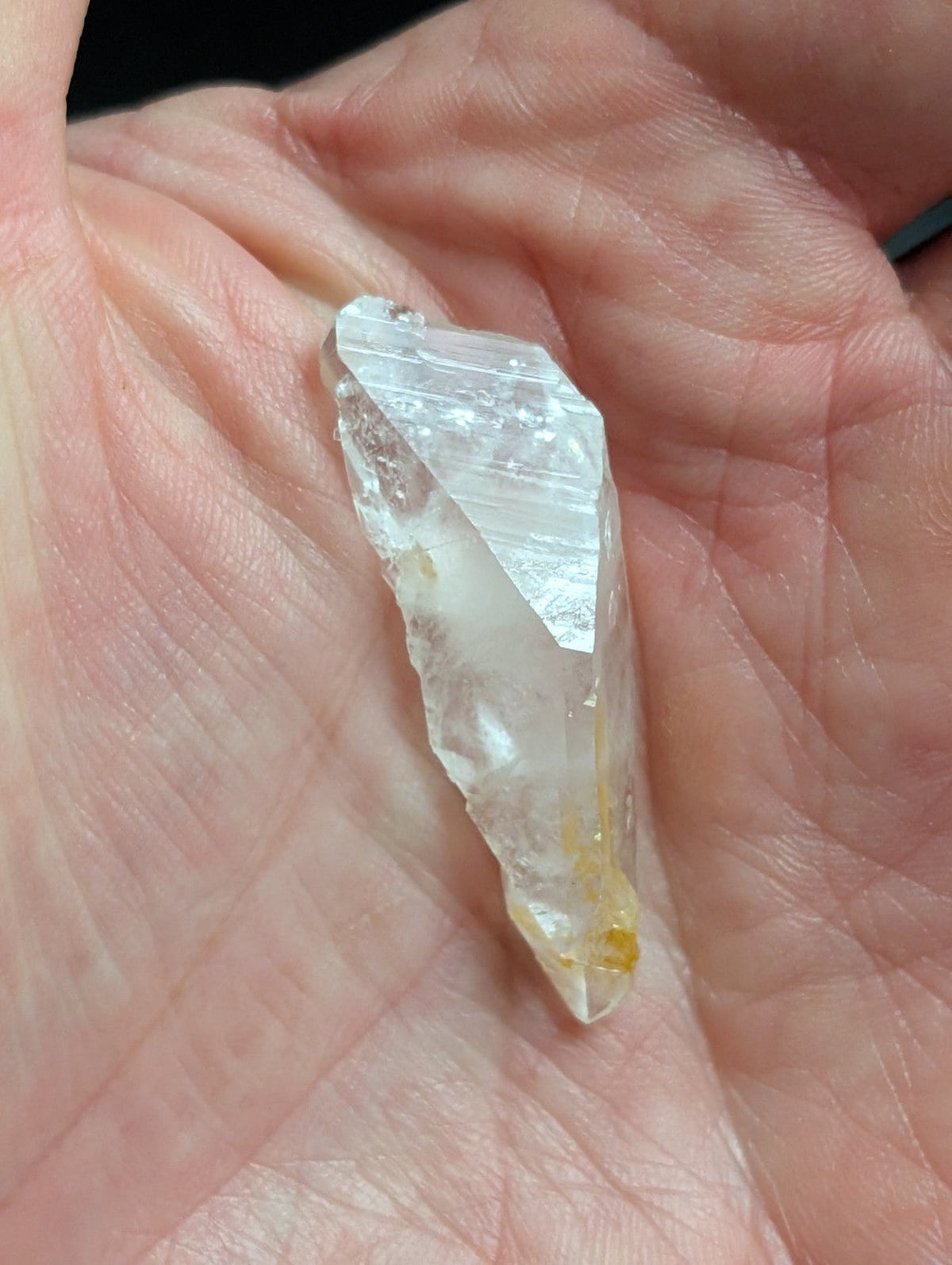 A translucent, clear quartz crystal with a pointed tip and subtle golden inclusions.