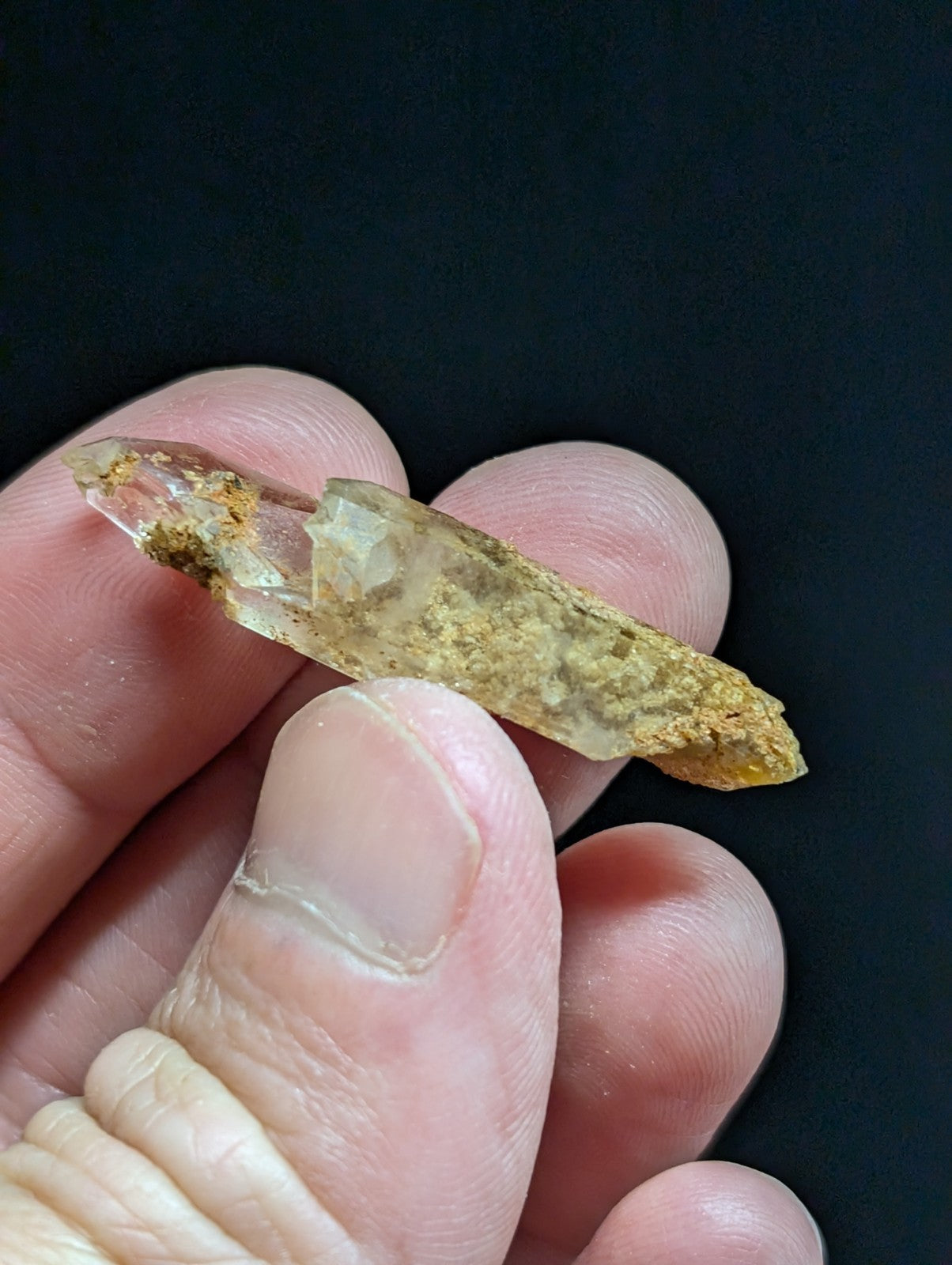 A translucent, amber-hued crystal with a pointed tip and rough, earthy surface held gently in someone’s hand.