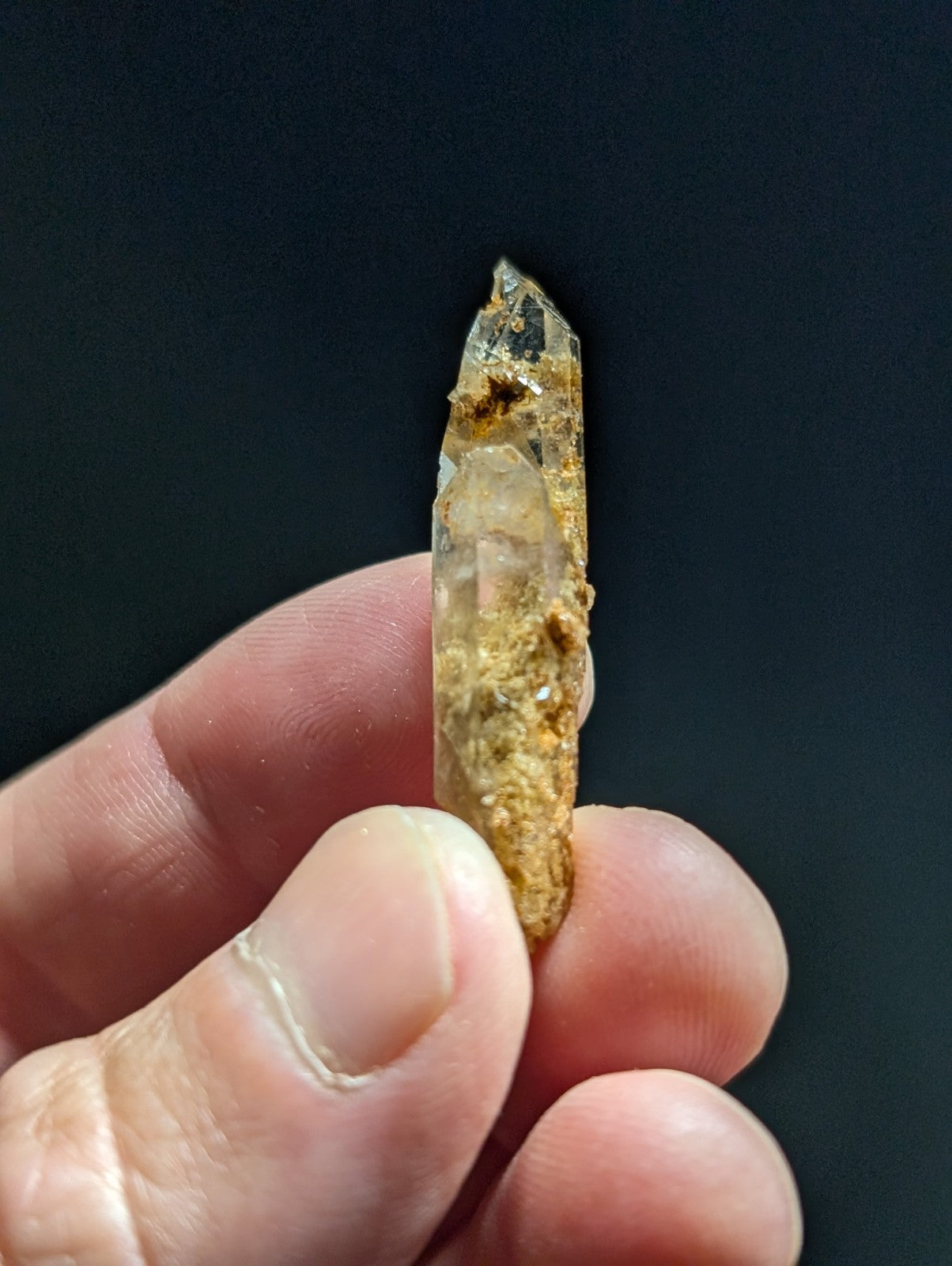 A translucent, amber-tinted quartz crystal with a pointed tip and visible mineral inclusions.