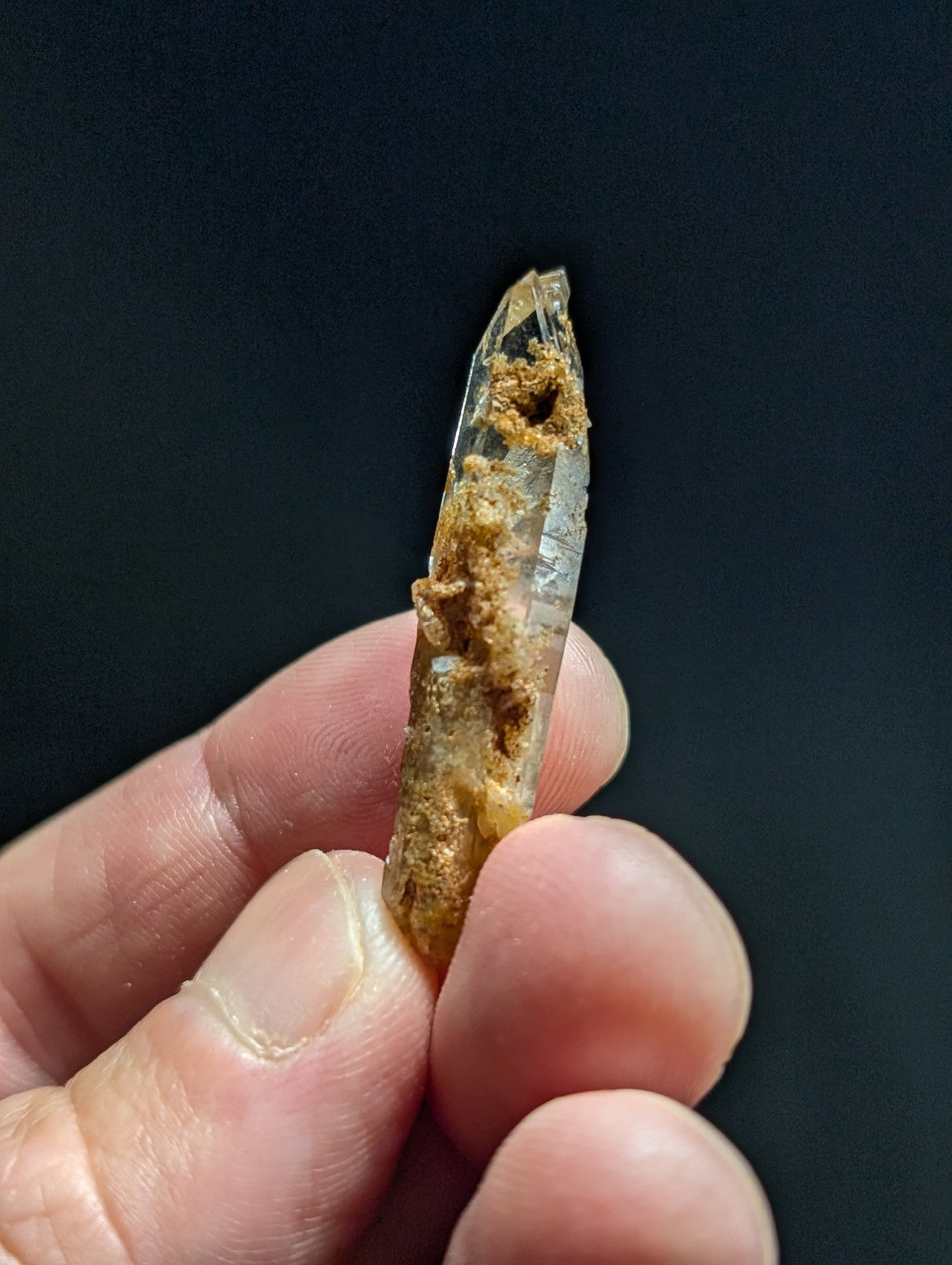 A translucent quartz crystal with a pointed tip, featuring natural brownish inclusions and rough textures along its length.