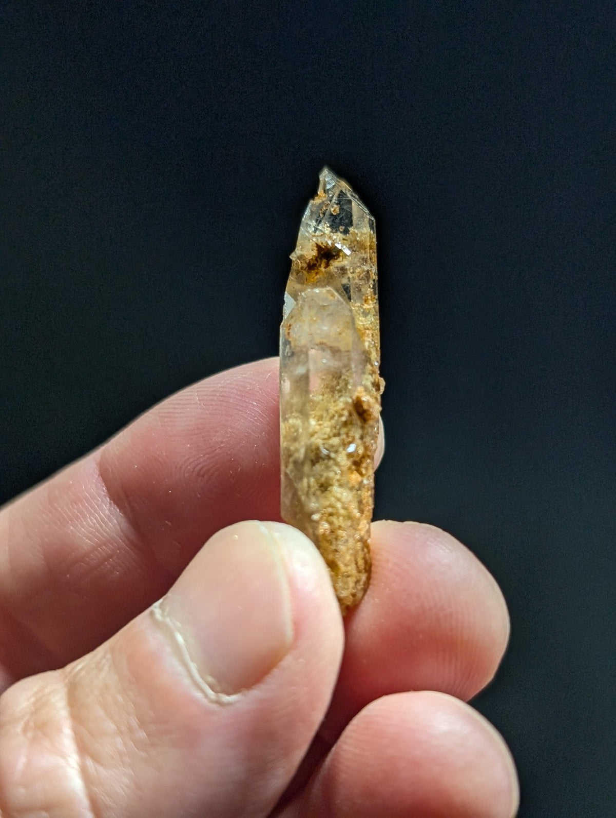 A translucent, amber-tinted quartz crystal with a pointed tip and visible mineral inclusions.