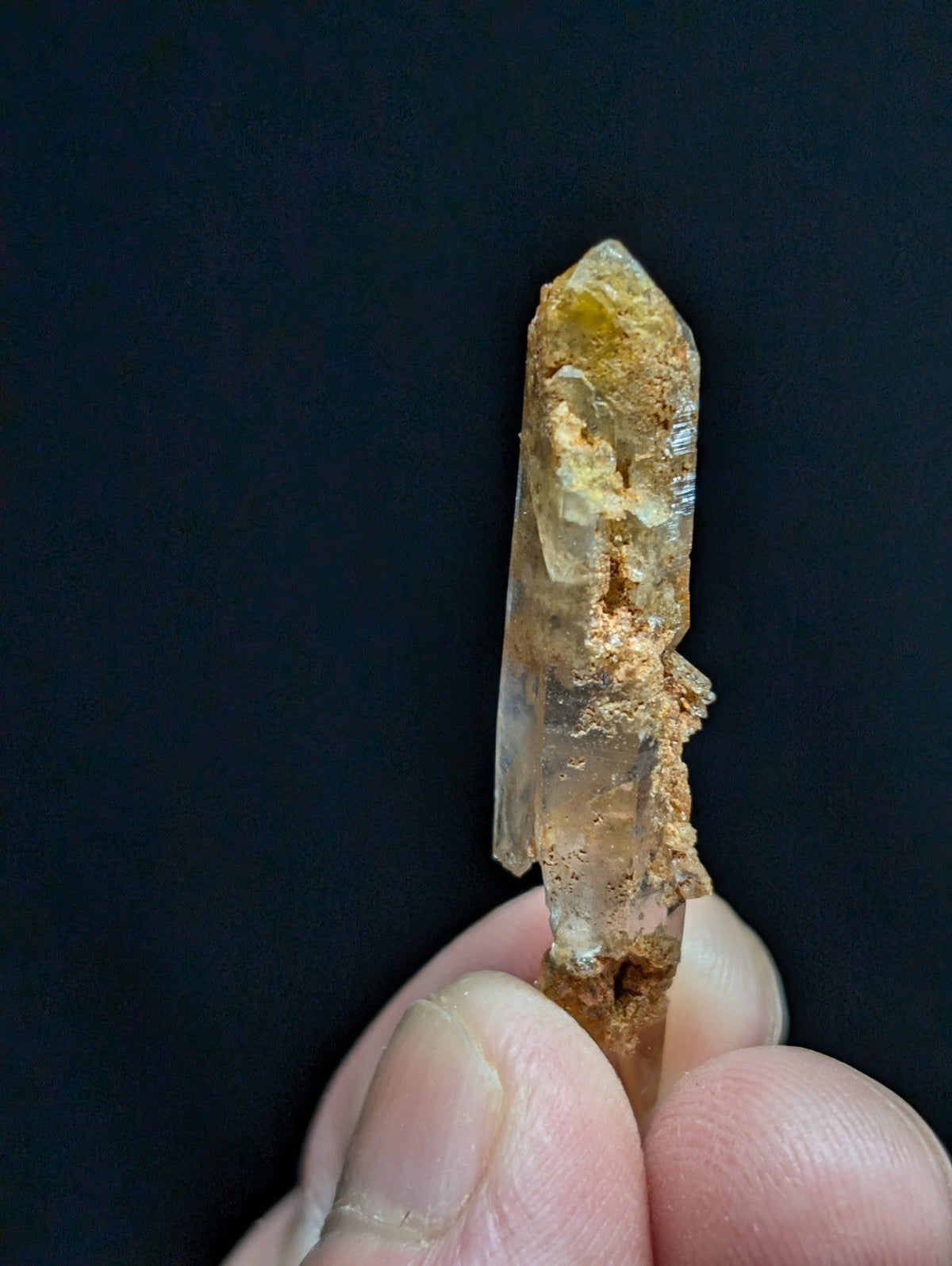 A translucent quartz crystal with a pointed tip, featuring natural amber and brown mineral inclusions along its surface.
