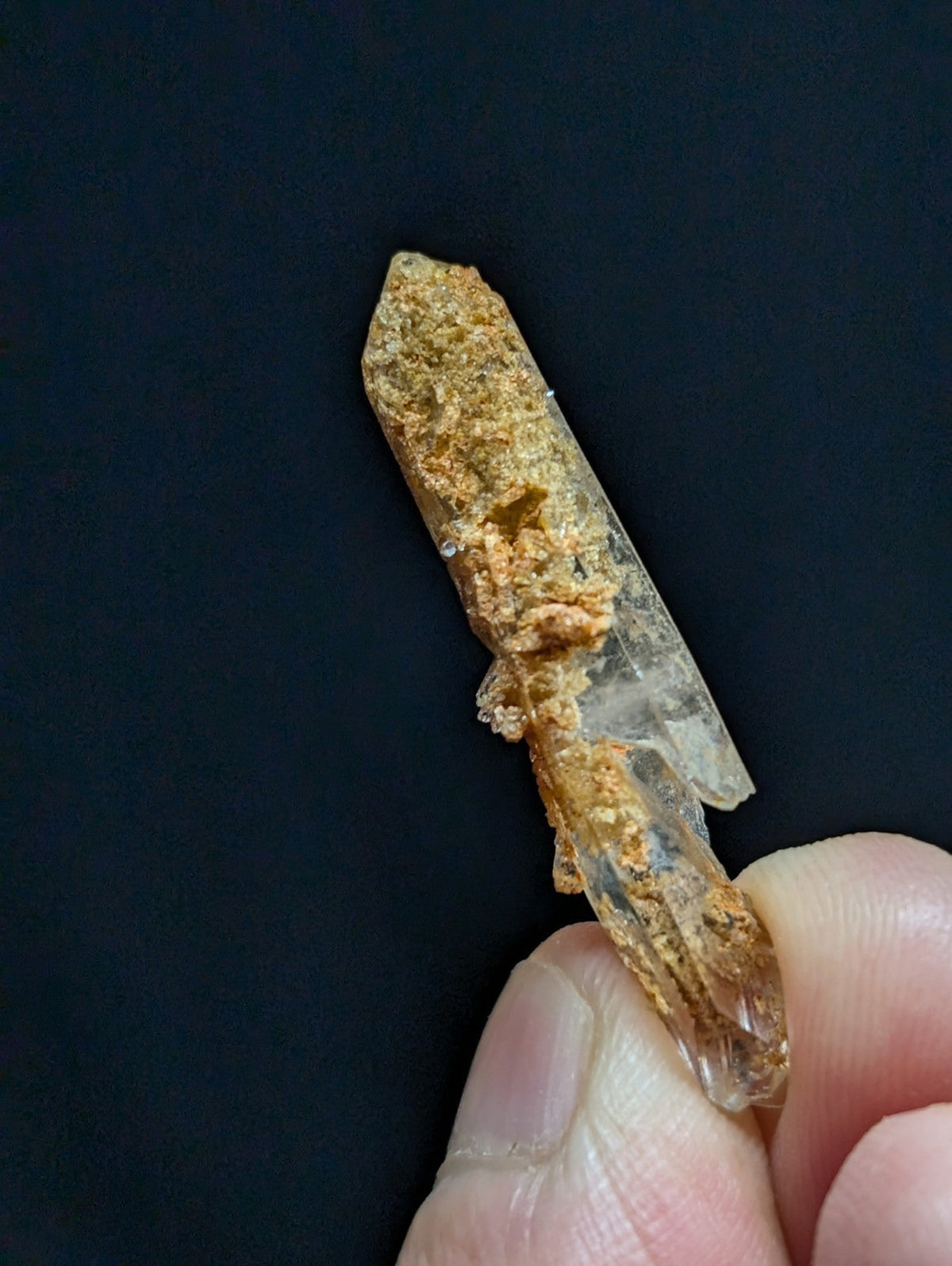 A translucent quartz crystal with a rough, earthy brown matrix clinging to its surface.