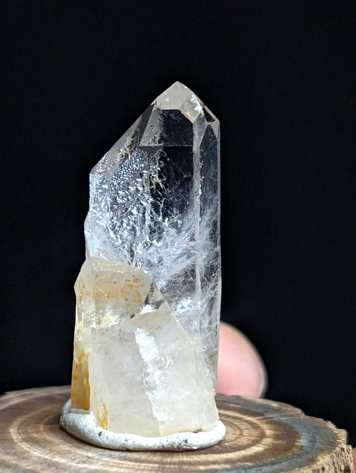 A clear, faceted quartz crystal with a translucent body and subtle golden inclusions at its base.