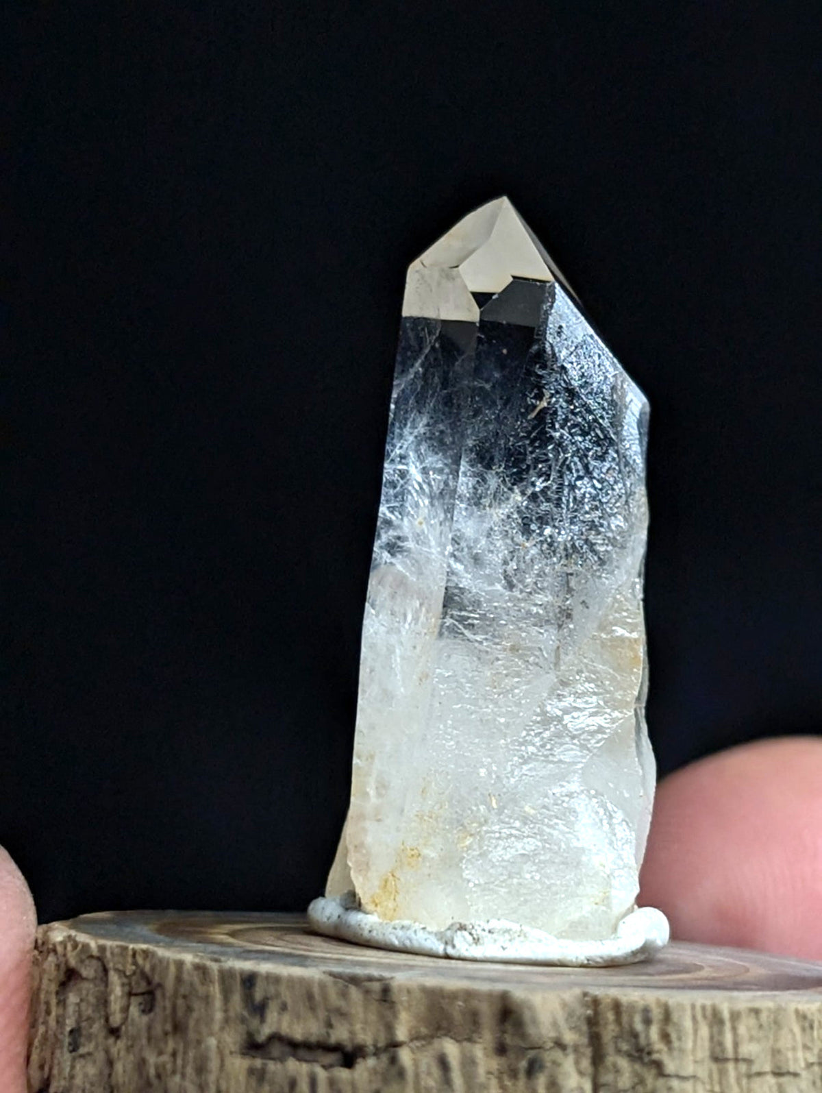 A clear, translucent quartz crystal with a pointed tip and subtle internal veining rests on a rustic wooden base.