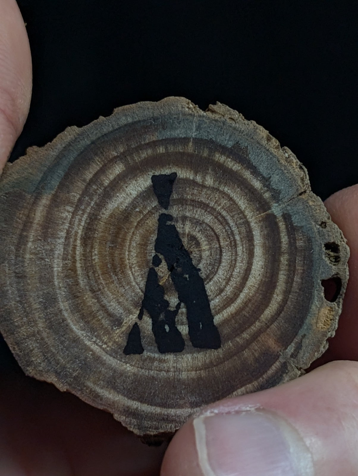 A rustic, circular wooden slice pendant featuring a black-painted silhouette of three figures in an embrace.