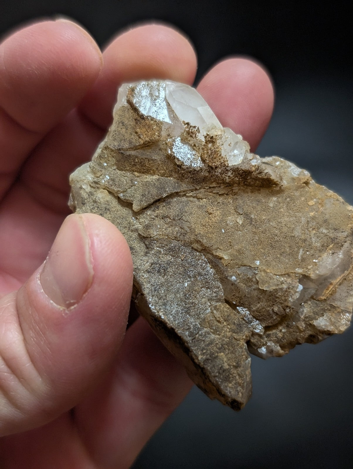 A translucent quartz crystal cluster embedded in a rough, earthy brown rock matrix.