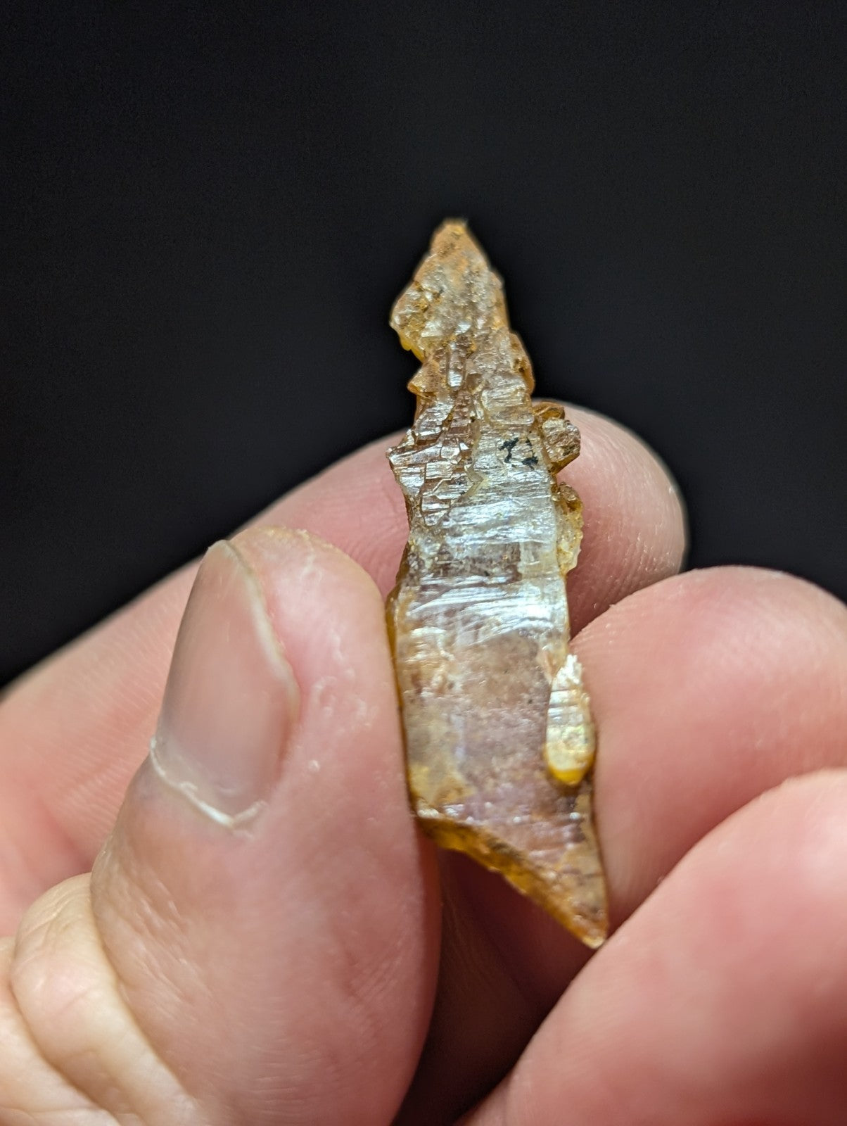 A translucent amber-colored crystal fragment with a jagged, natural edge and visible internal striations.