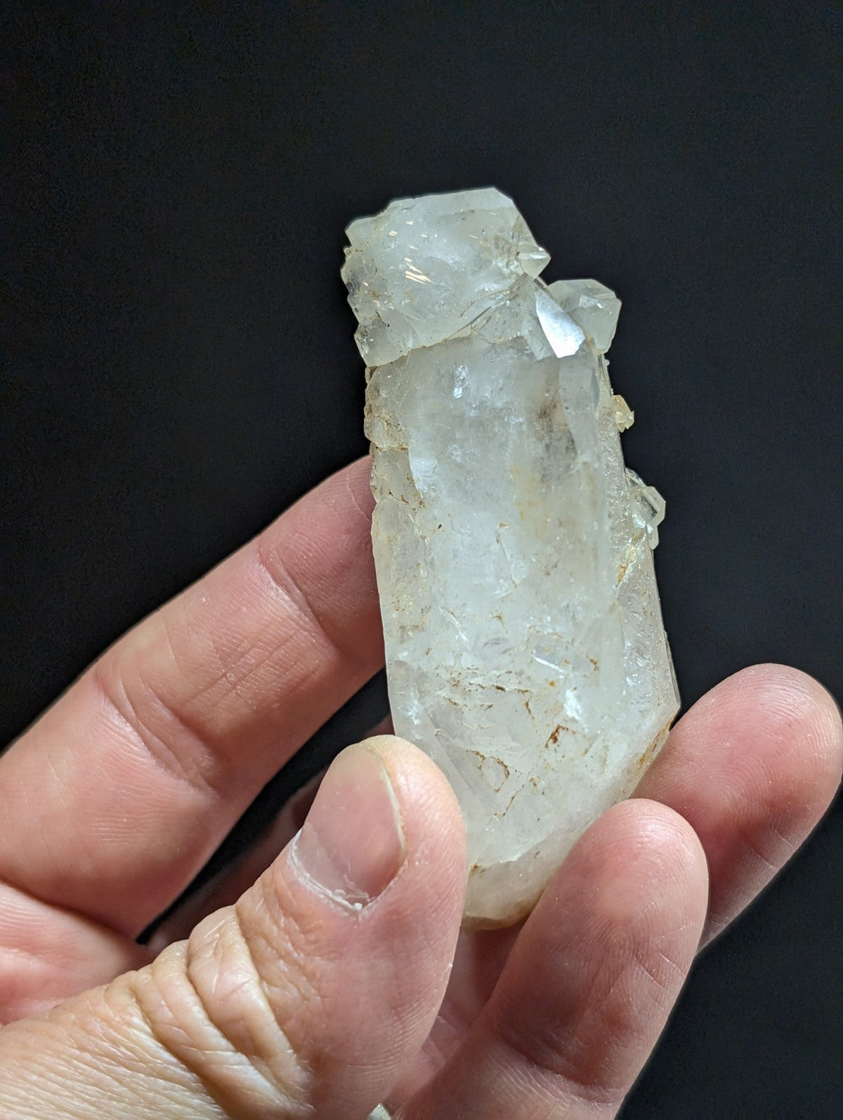 A translucent, clear quartz crystal with a rough, jagged top and smooth, faceted sides.