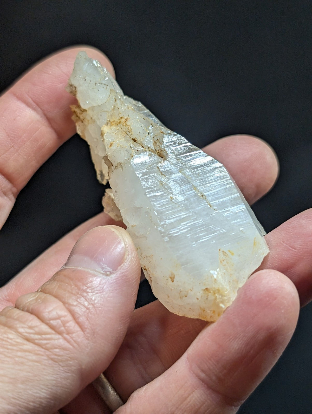 A translucent white quartz crystal with visible striations and some yellowish mineral inclusions, held gently between fingers.