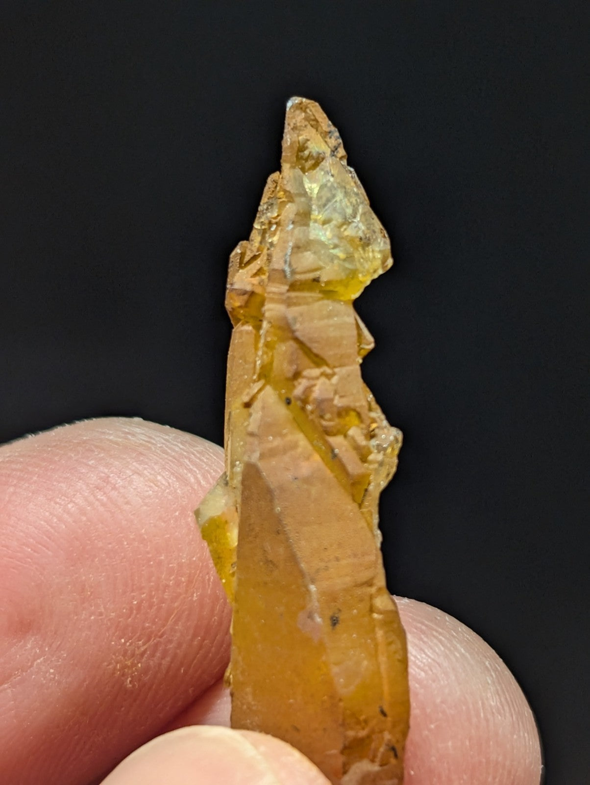 A translucent amber-colored crystal with a jagged, pointed tip and natural facets.