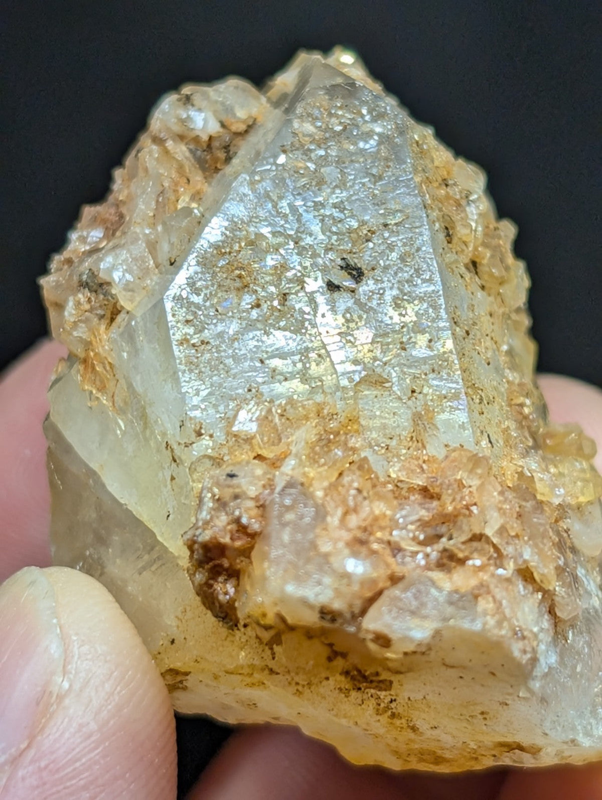A translucent, golden-hued quartz crystal with a faceted surface and embedded mineral inclusions.