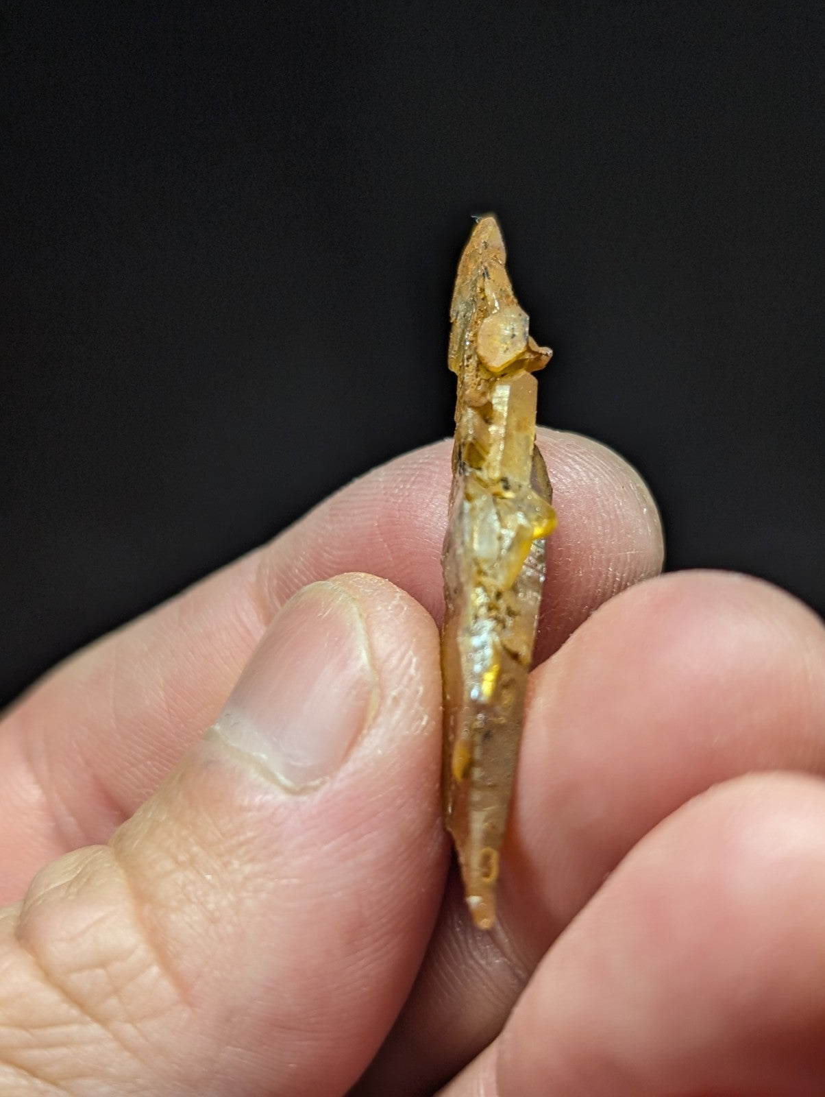 A translucent golden-yellow crystal with a pointed tip and natural, rough edges.