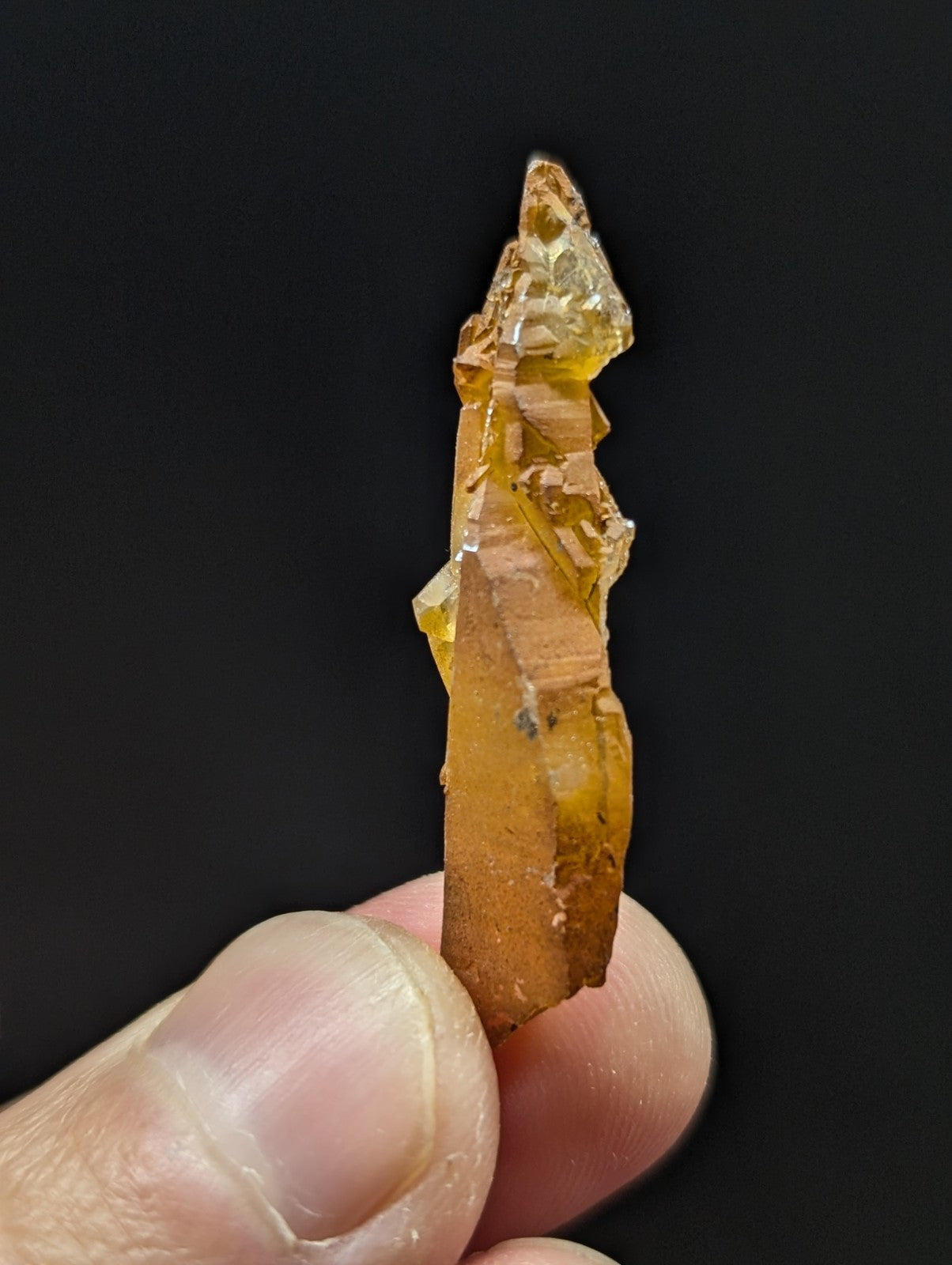 A translucent amber-colored crystal with a jagged, pointed top and layered internal structure.