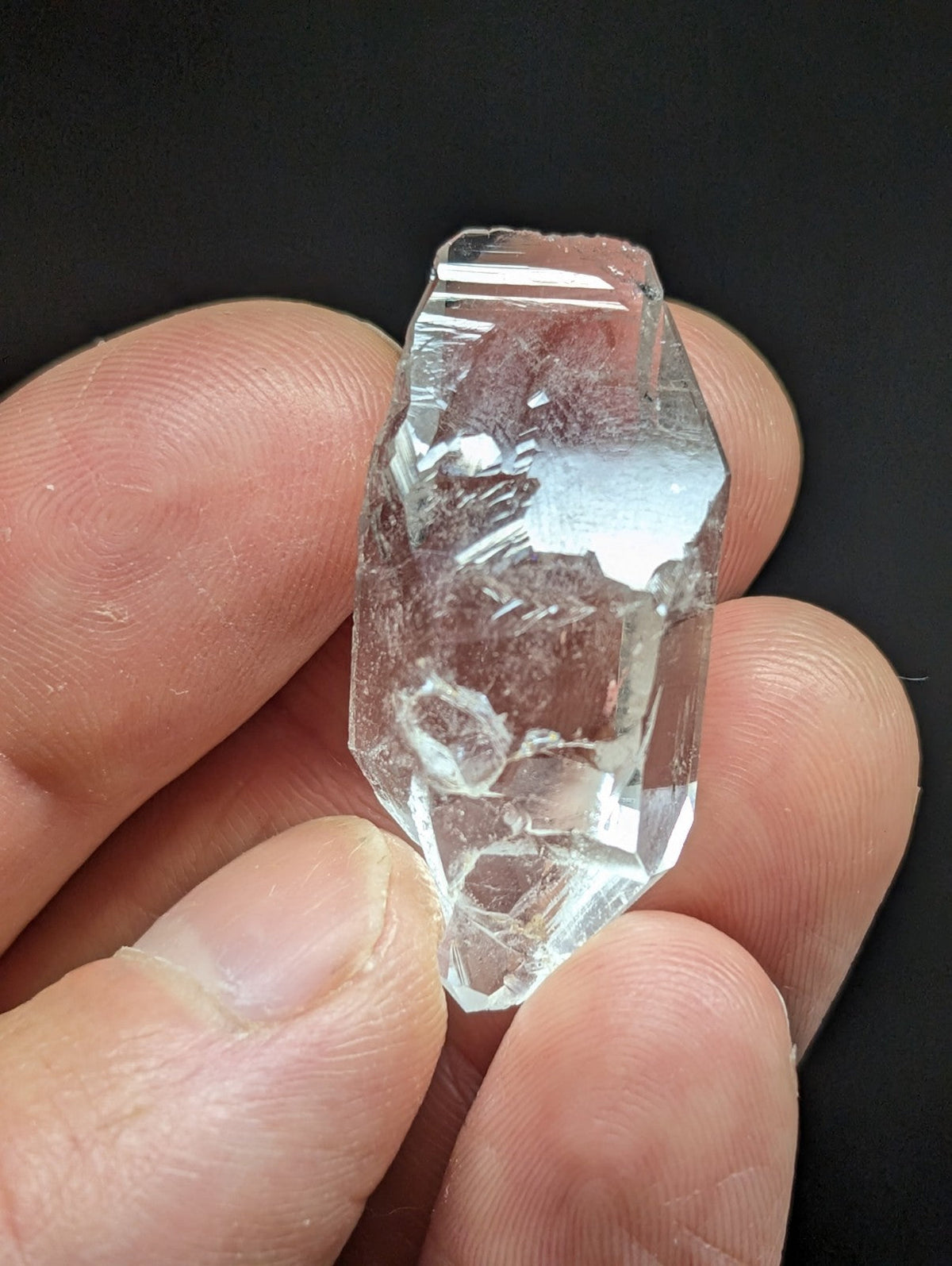 A clear, faceted quartz crystal with natural internal inclusions and a rough, jagged surface.