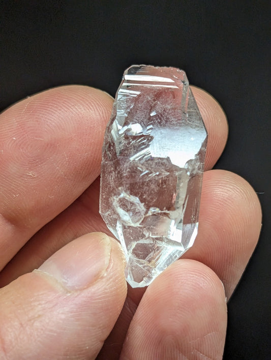 A clear, faceted quartz crystal with natural internal inclusions and a rough, jagged surface.