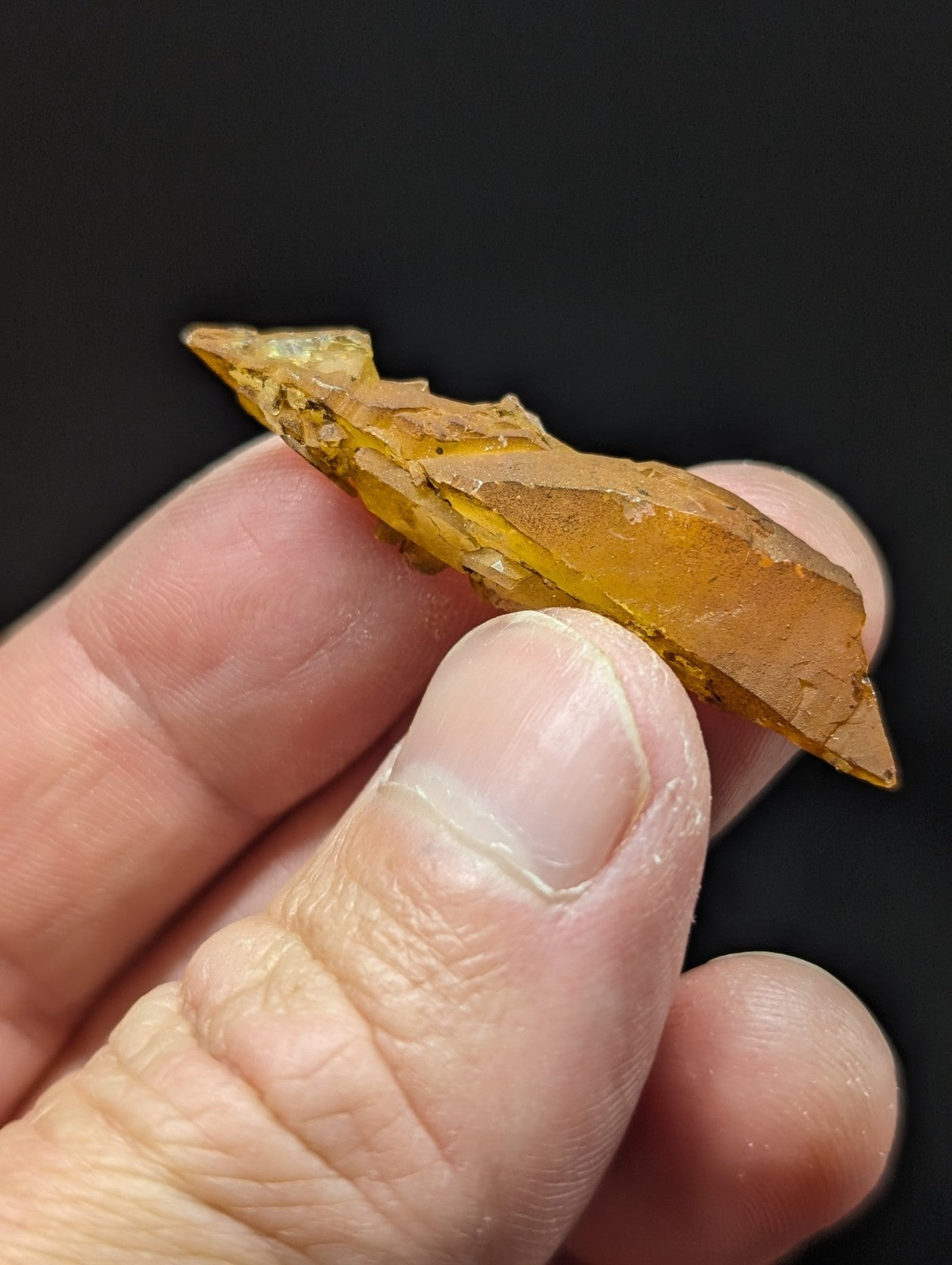 A translucent amber-colored, irregularly shaped crystal fragment with a glossy surface and natural facets.