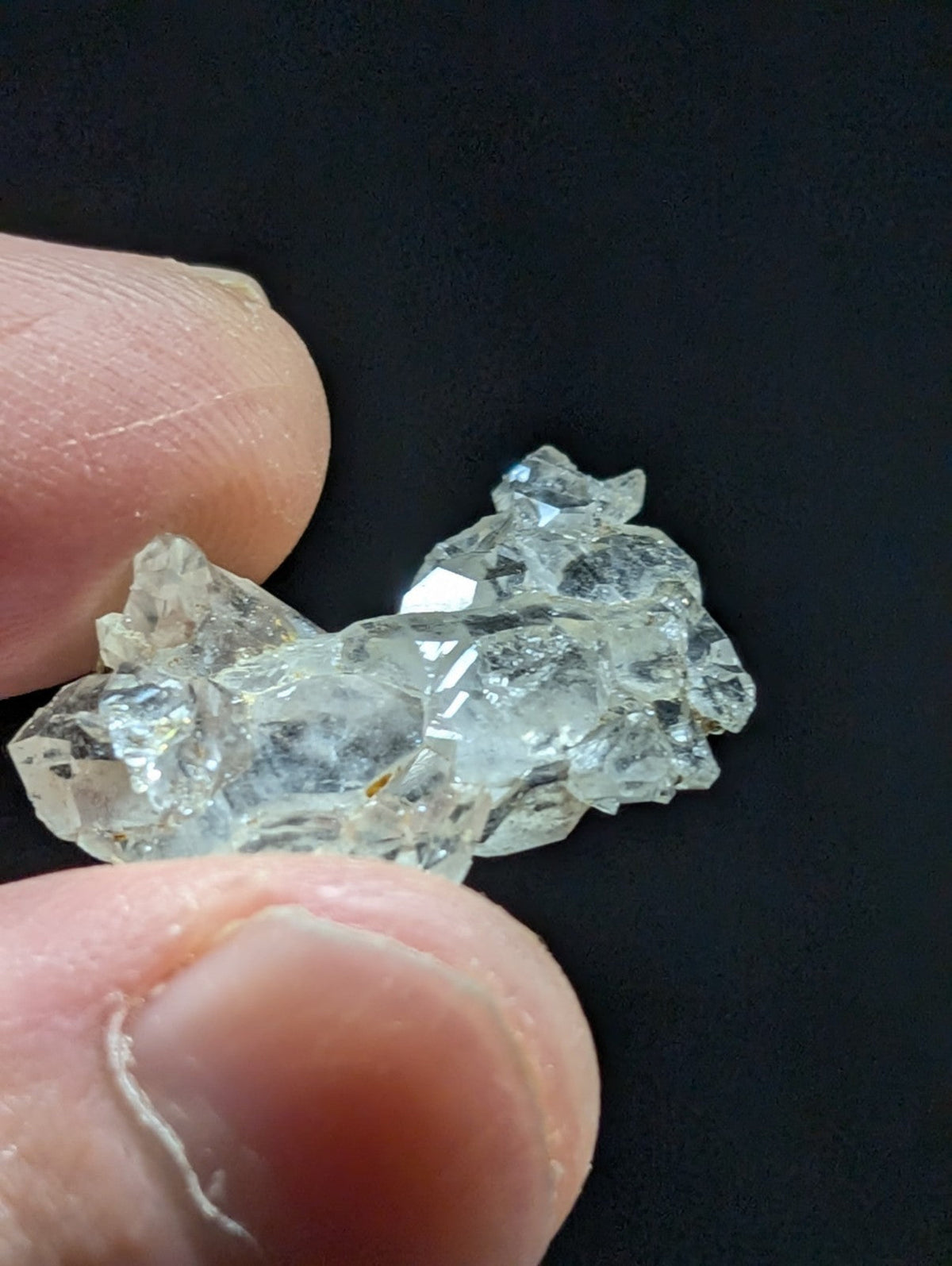 A clear, faceted quartz crystal cluster held between fingers.